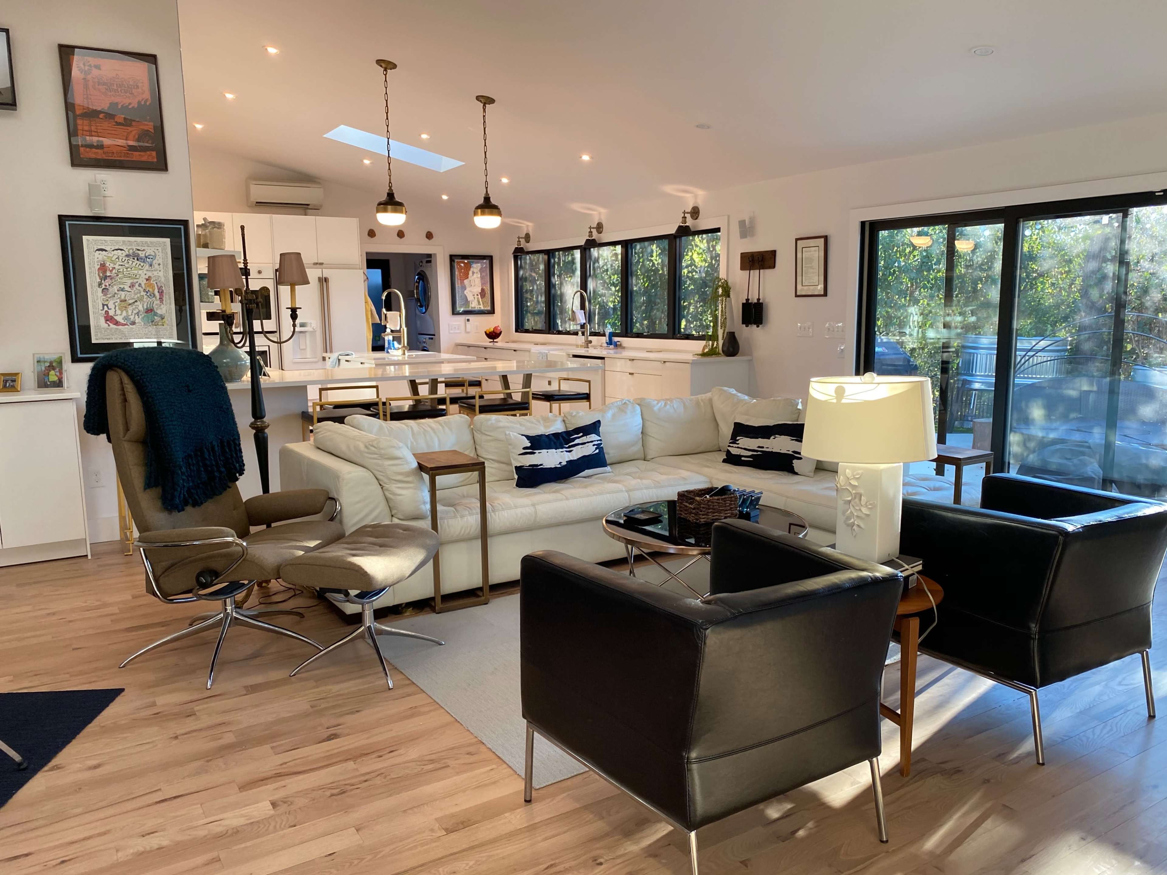 A modern, open-concept living room with a white sectional sofa, two black armchairs, and a wooden dining area in the background.