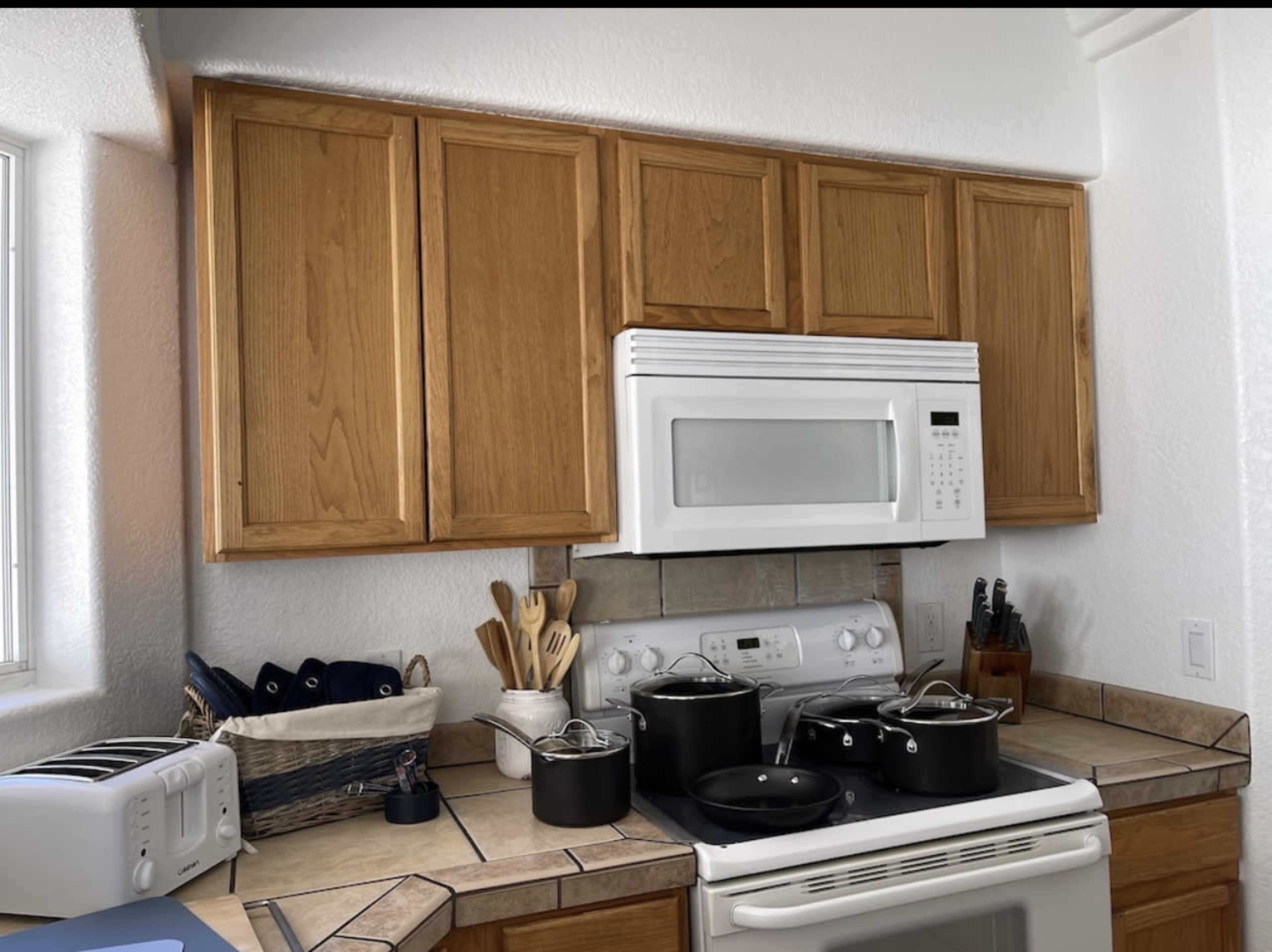 The image shows a kitchen with wooden cabinets above a white microwave and stove, featuring various pots and utensils arranged on the countertop.