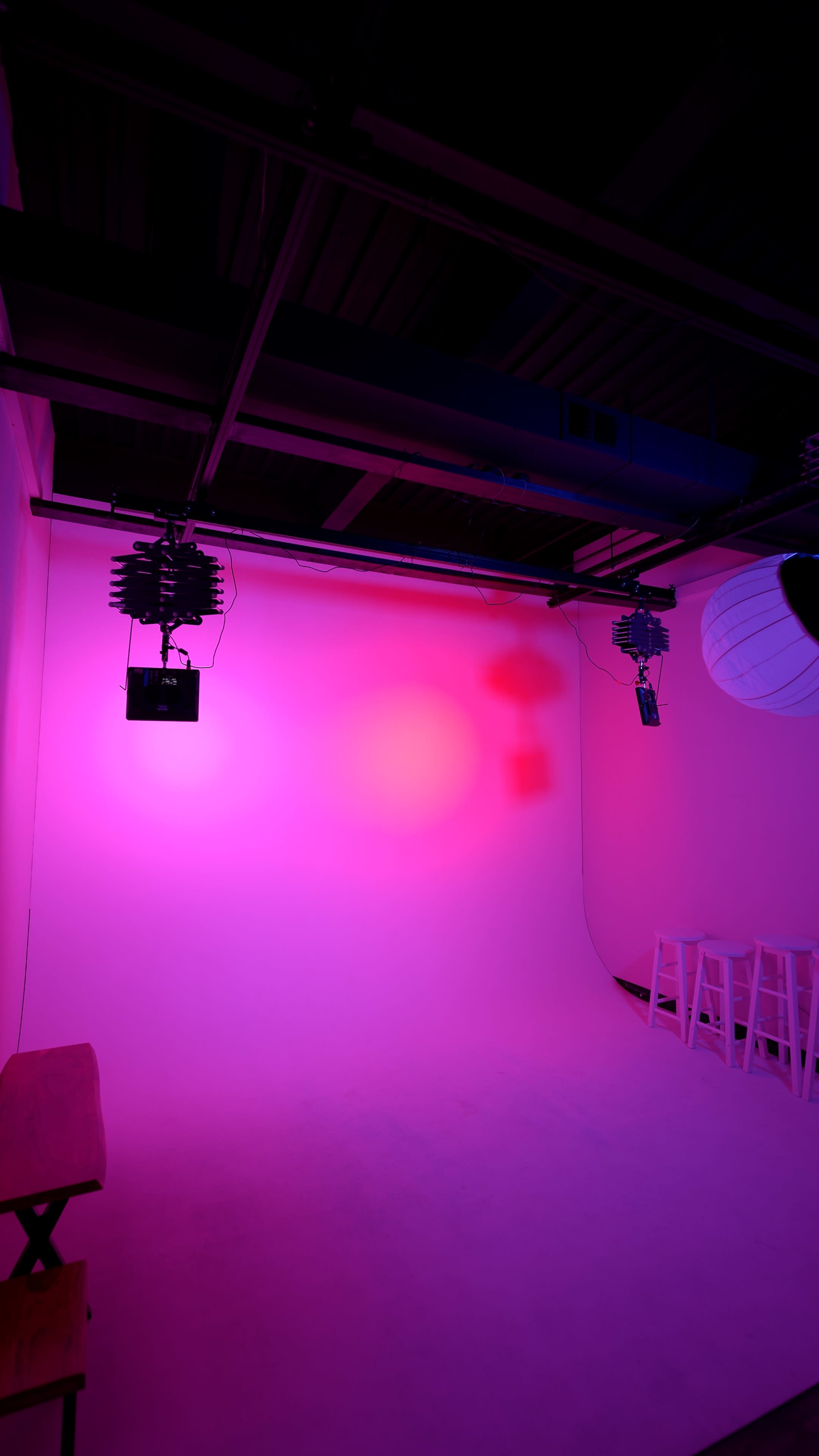 The image shows a studio space with pink lighting, featuring a seamless backdrop and mounted lighting equipment.