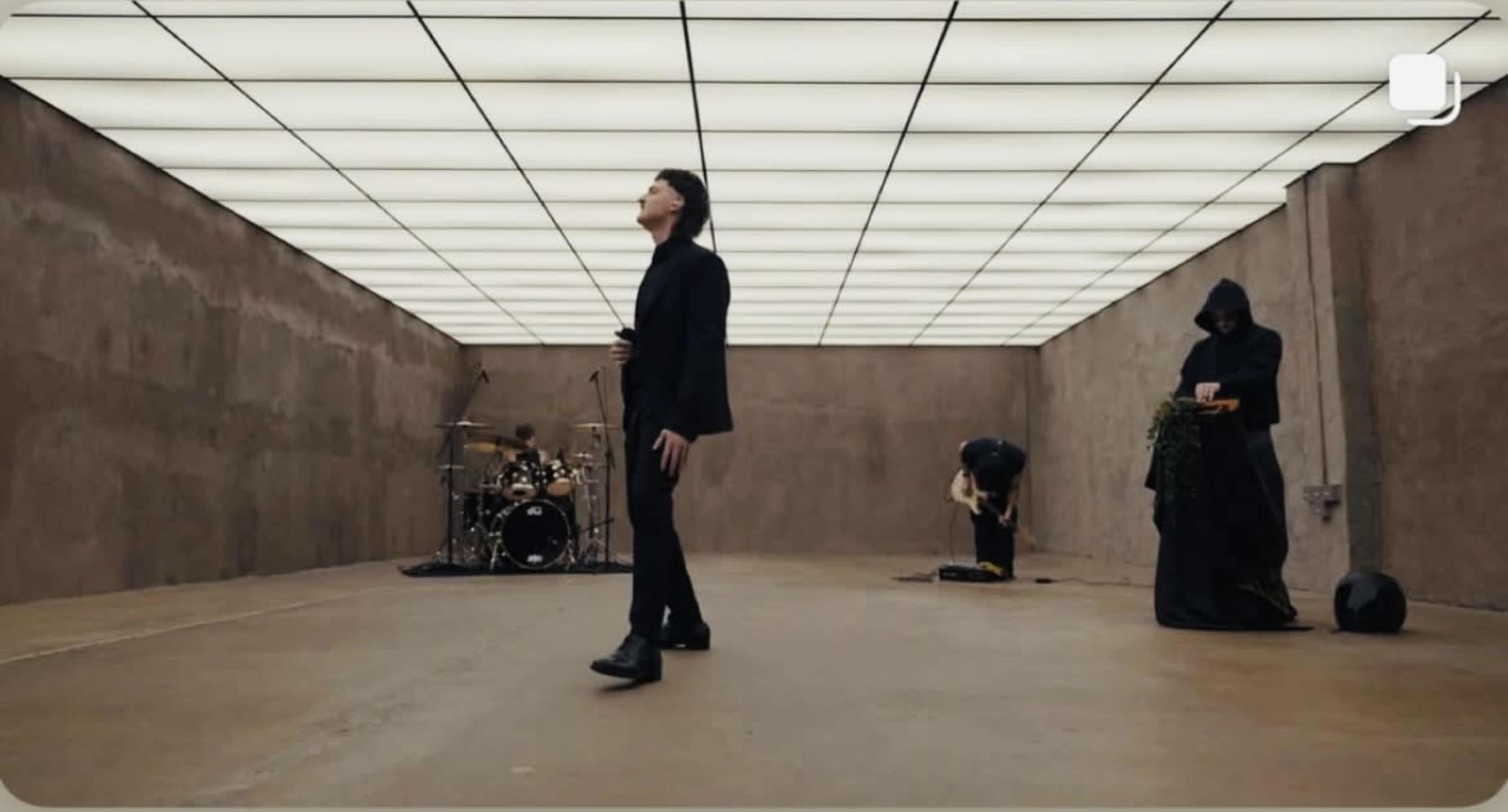 A band performs in a sparse, well-lit room with a smooth floor and concrete walls.