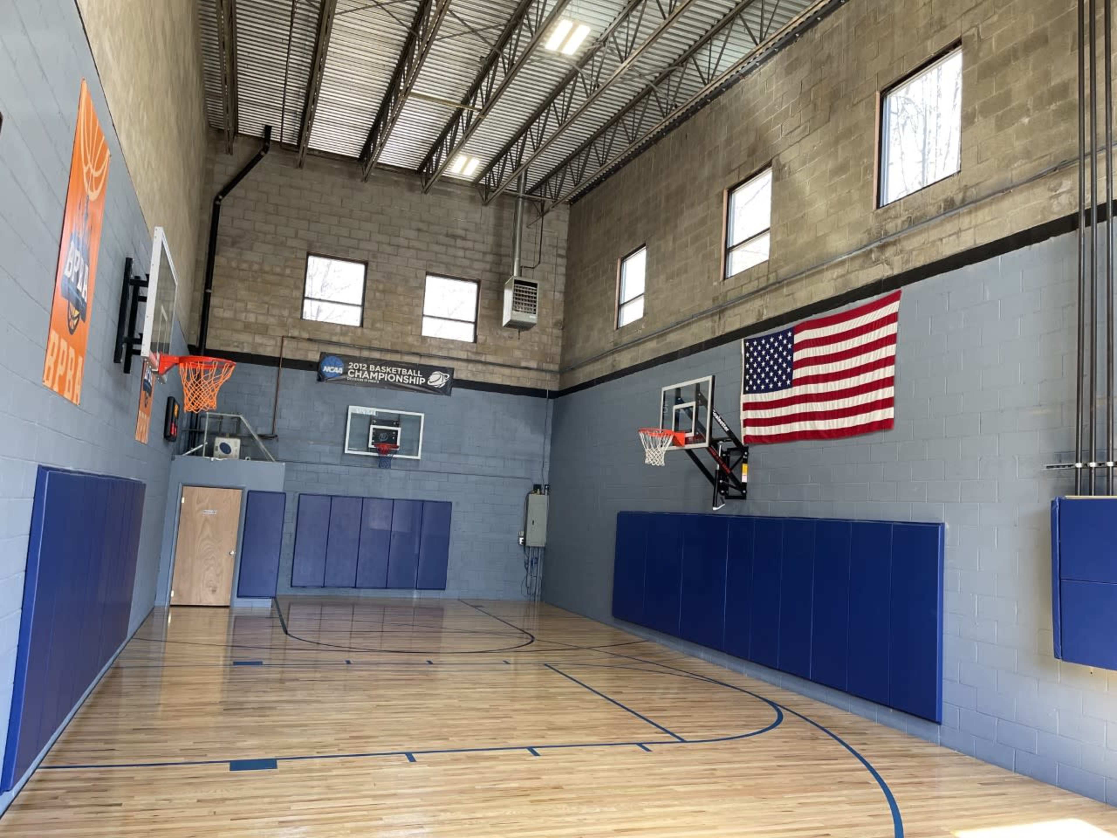A basketball gym with two hoops, a blue wall, and an American flag hanging on the right side.