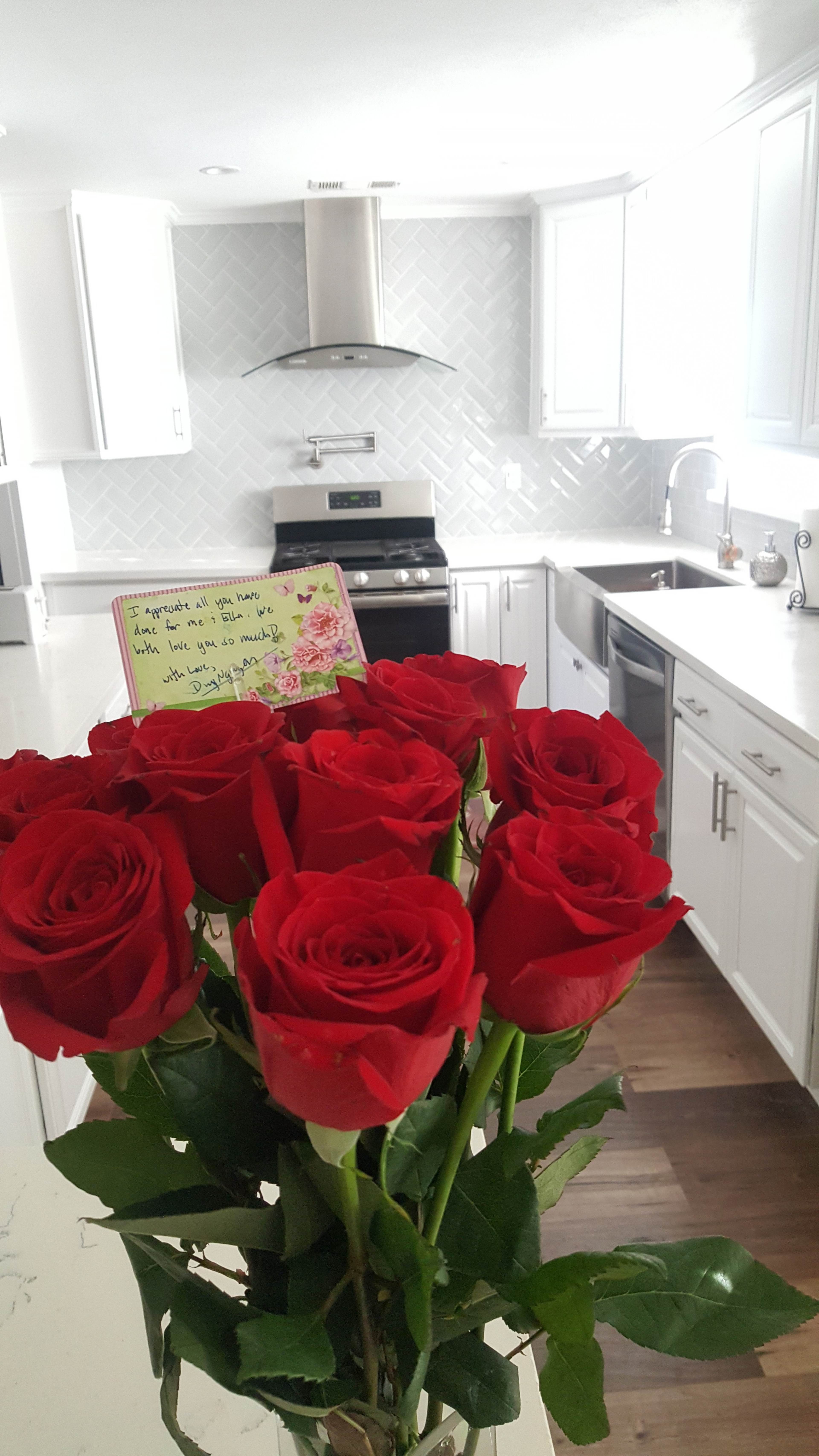 A bouquet of red roses is prominently displayed in the foreground of a bright and modern kitchen.