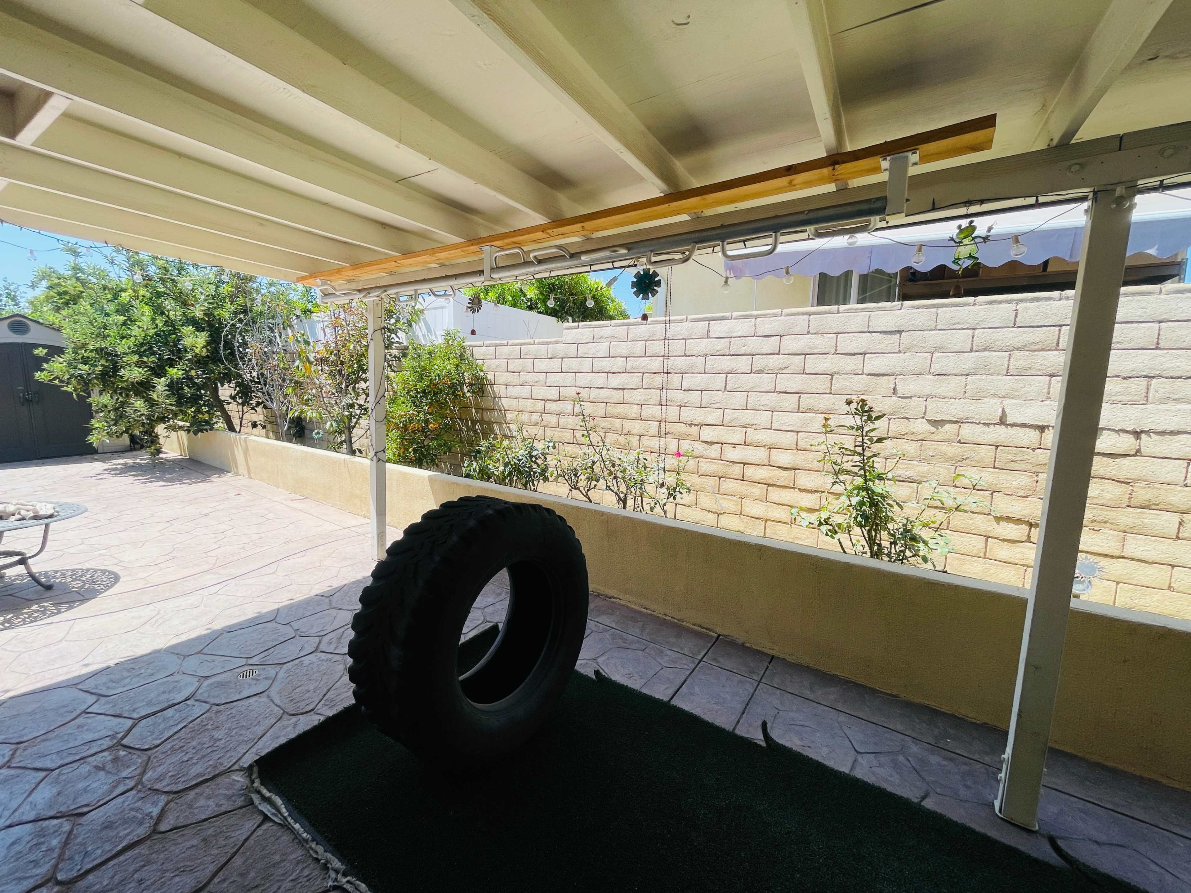 A view of a patio area with a large tire resting on a green mat and a garden against a stone wall in the background.
