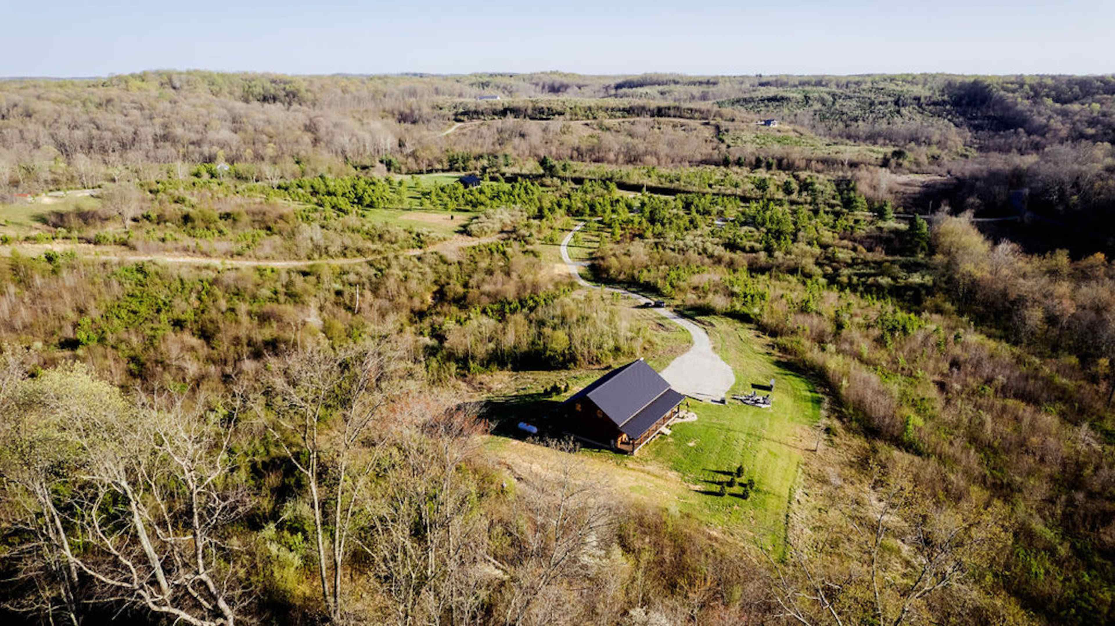 A wooden cabin sits surrounded by rolling hills and sparse trees, with a winding gravel path leading up to it.