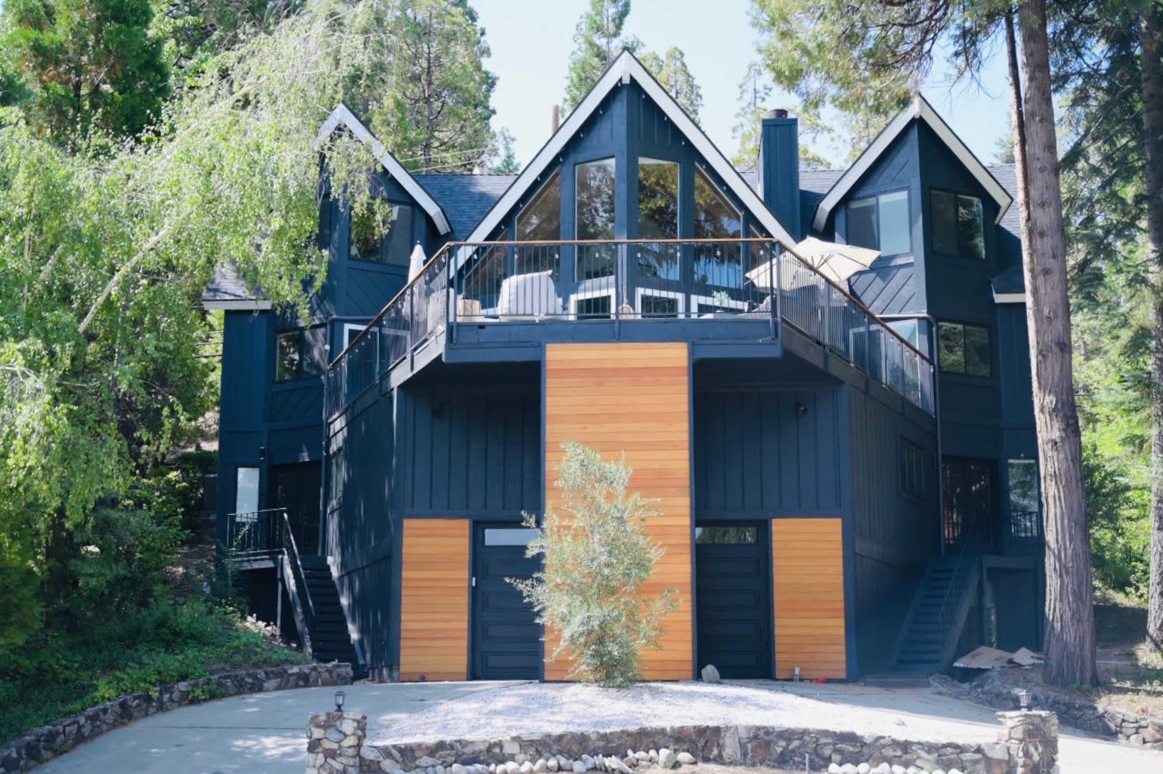 A large, modern black house with wooden accents and multiple levels is surrounded by trees and features a large balcony.