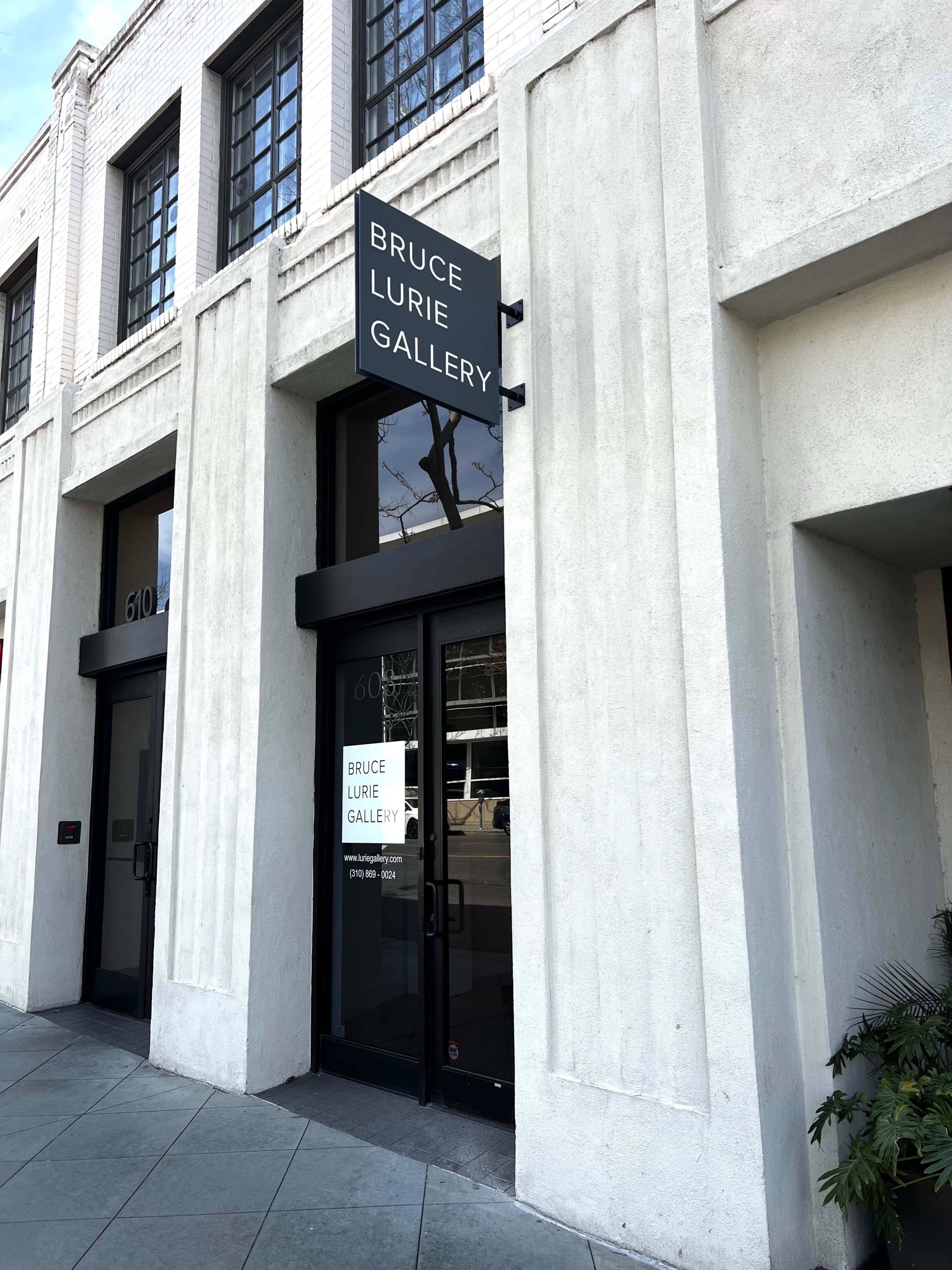 The image shows the entrance of the Bruce Lurie Gallery, featuring a large sign above the door and a glass facade.