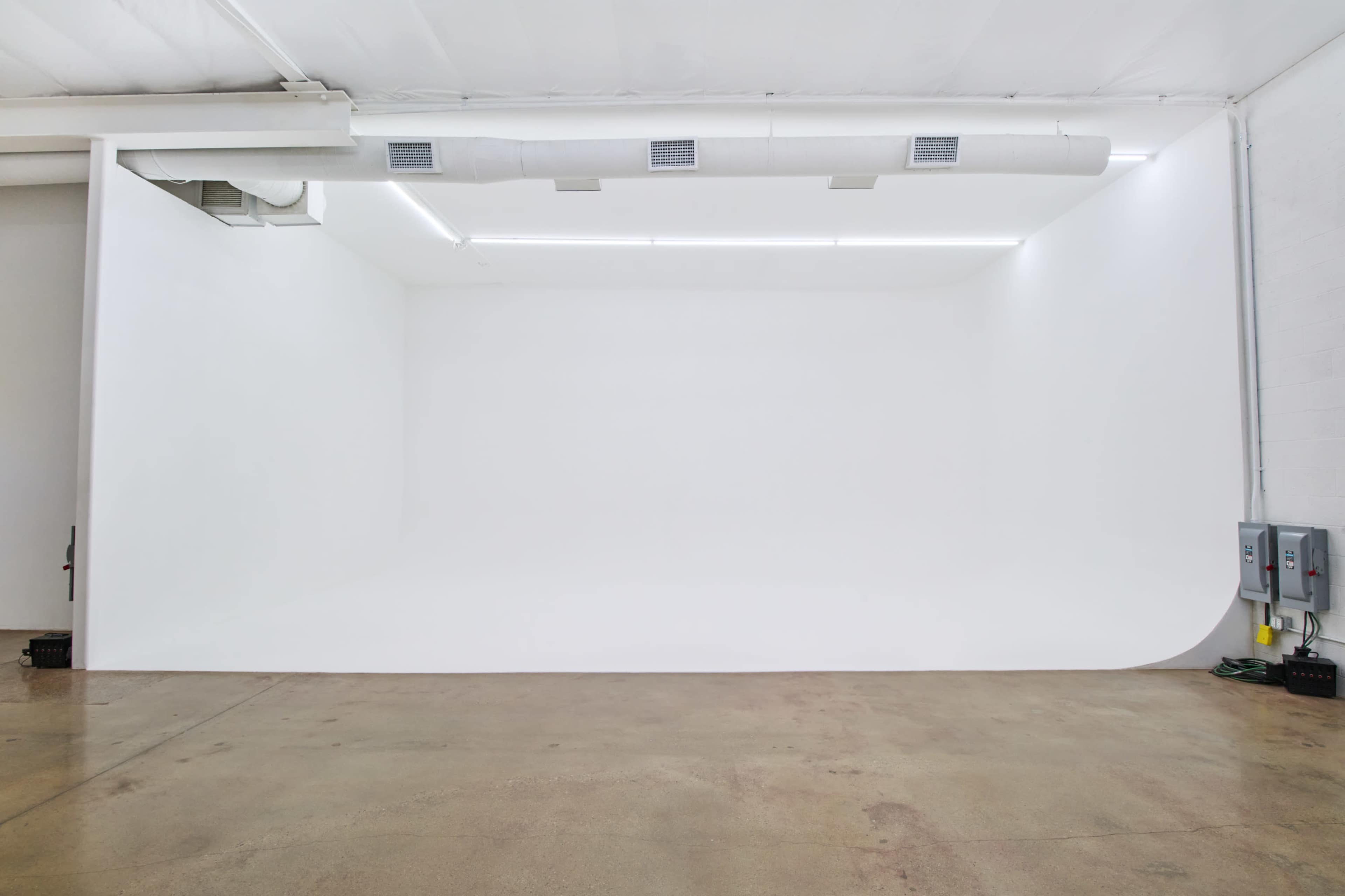 The image shows an empty white studio space with a seamless backdrop and concrete flooring.