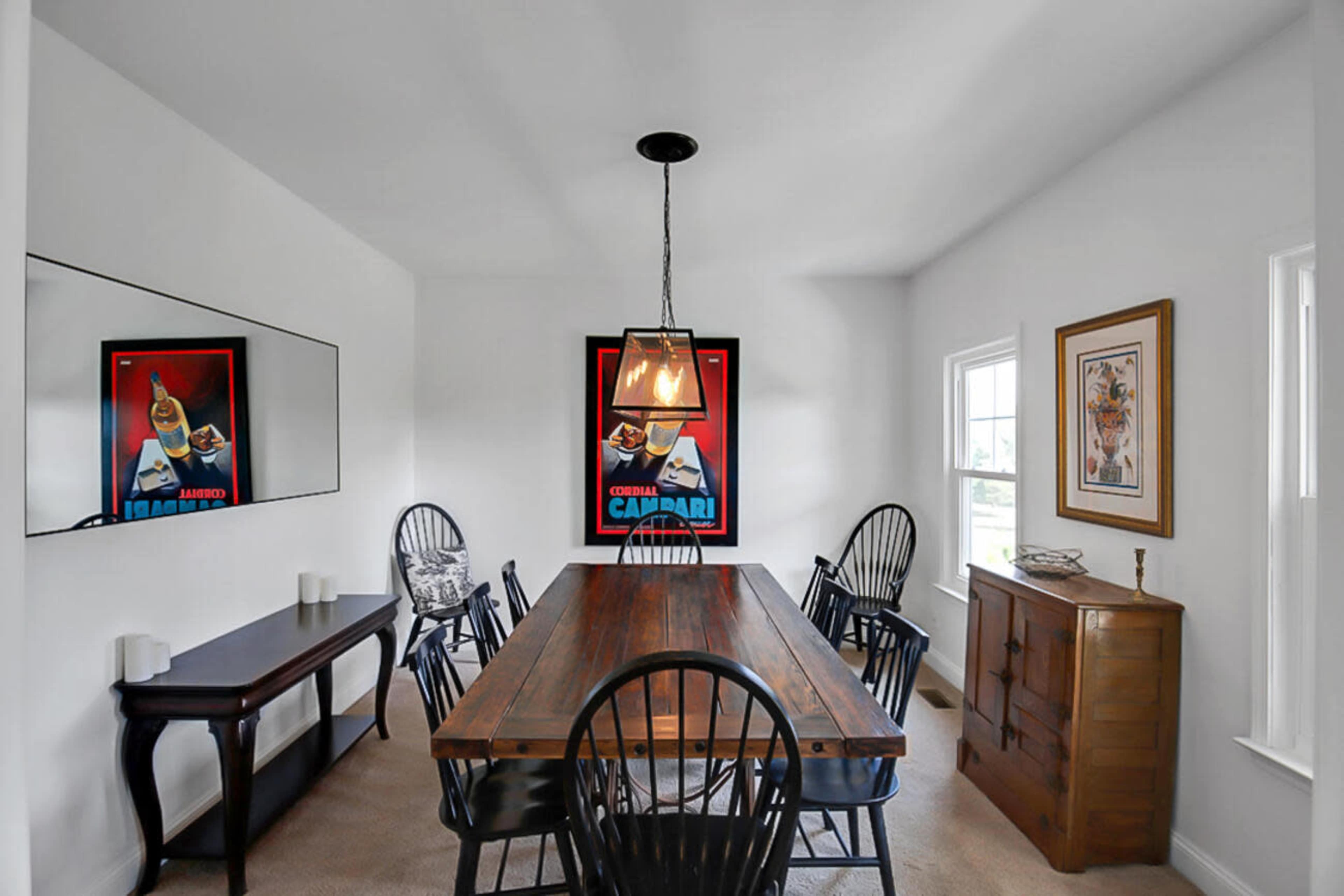 A modern dining room features a long wooden table surrounded by six black chairs, with decorative artwork on the walls and a sideboard in the corner.