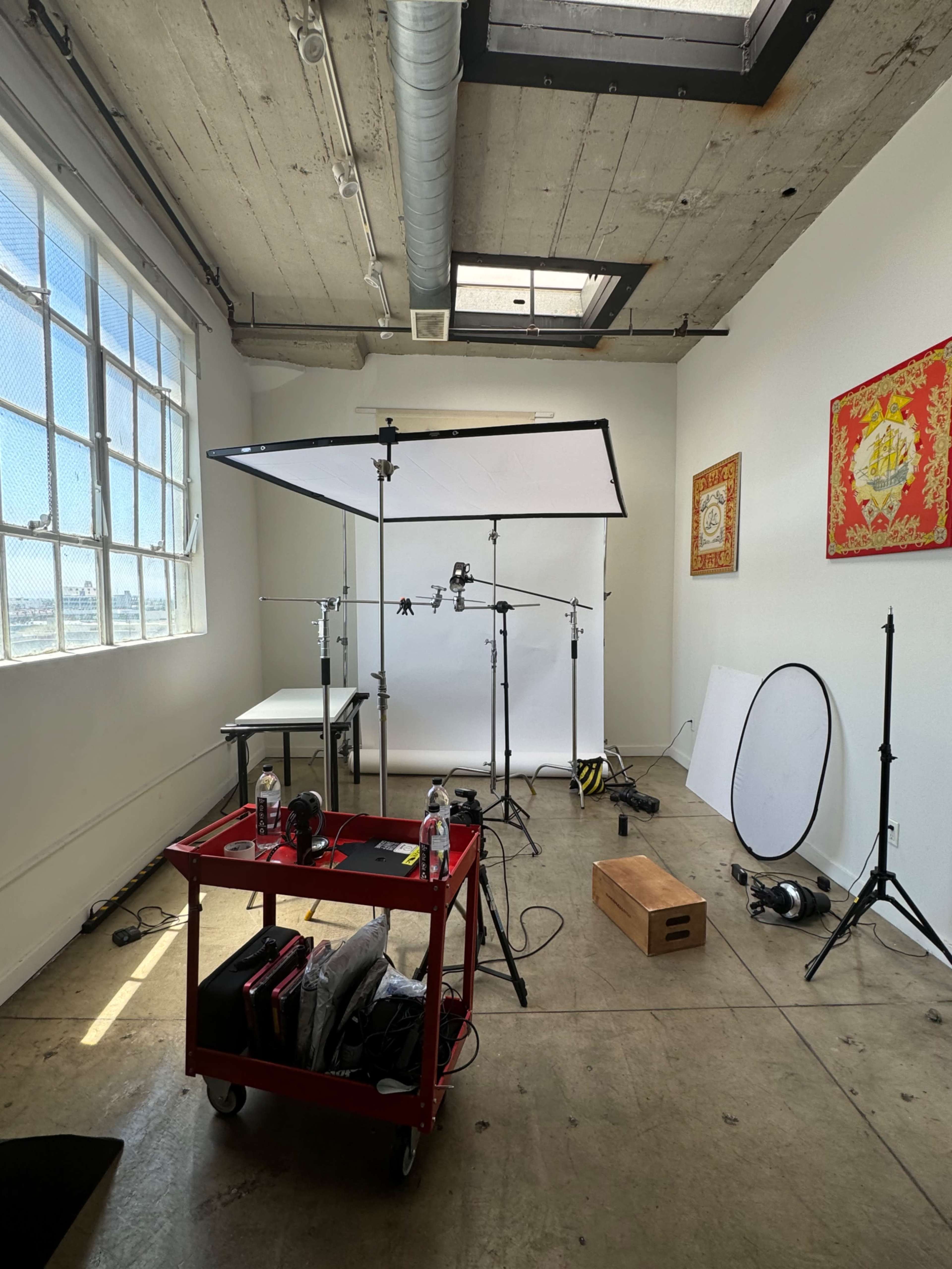 A photography studio with various lighting equipment, a table, and a red cart containing supplies.