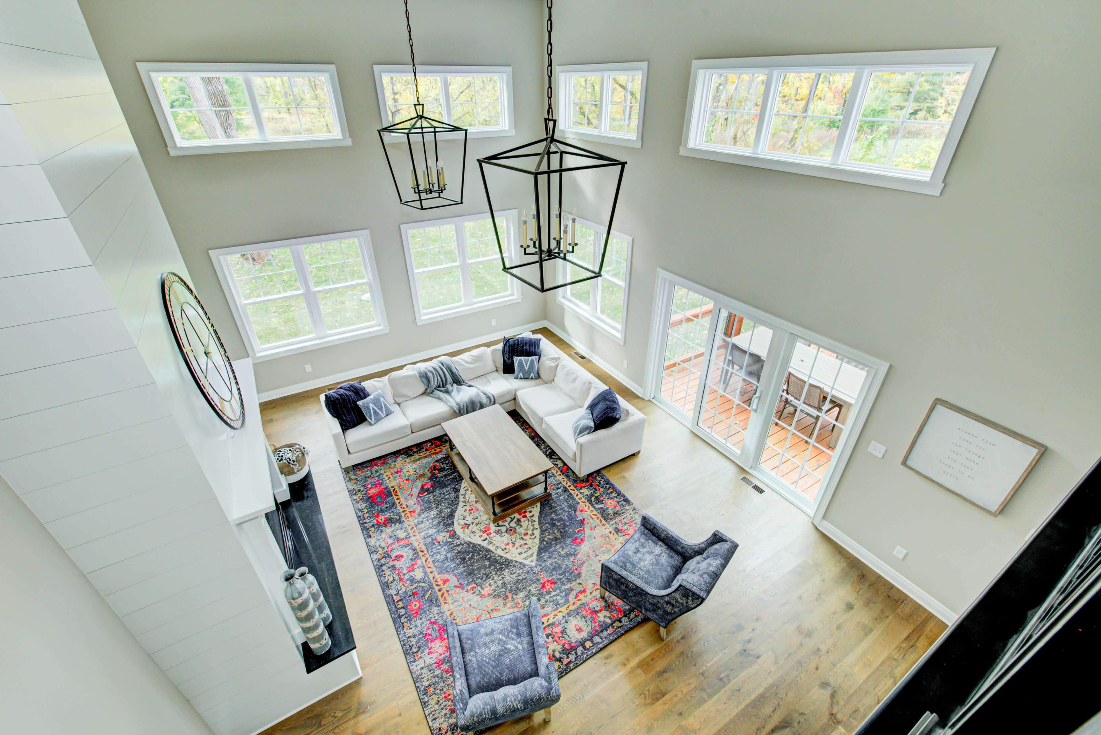 A spacious living room with large windows, a central coffee table, a rug, and comfortable seating arranged around it.