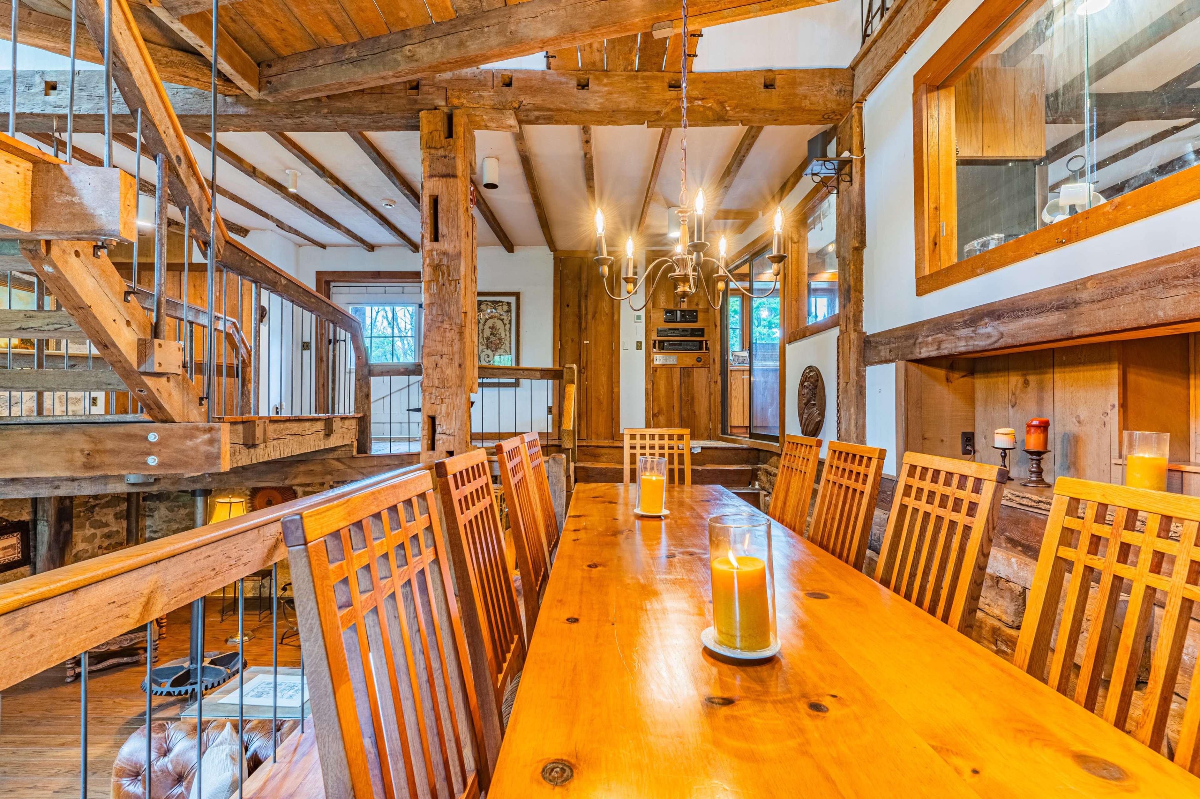 A rustic dining area with a long wooden table surrounded by slatted chairs and large wooden beams overhead.