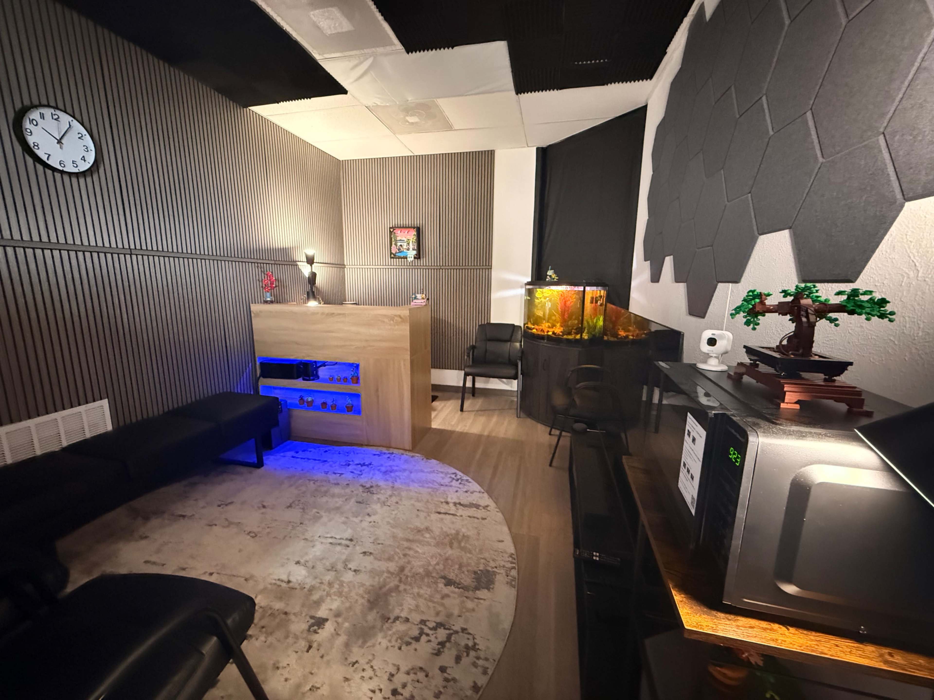 The image shows a modern room with a wooden reception desk, an aquarium, a couch, and decorative elements, including wall art and a clock.