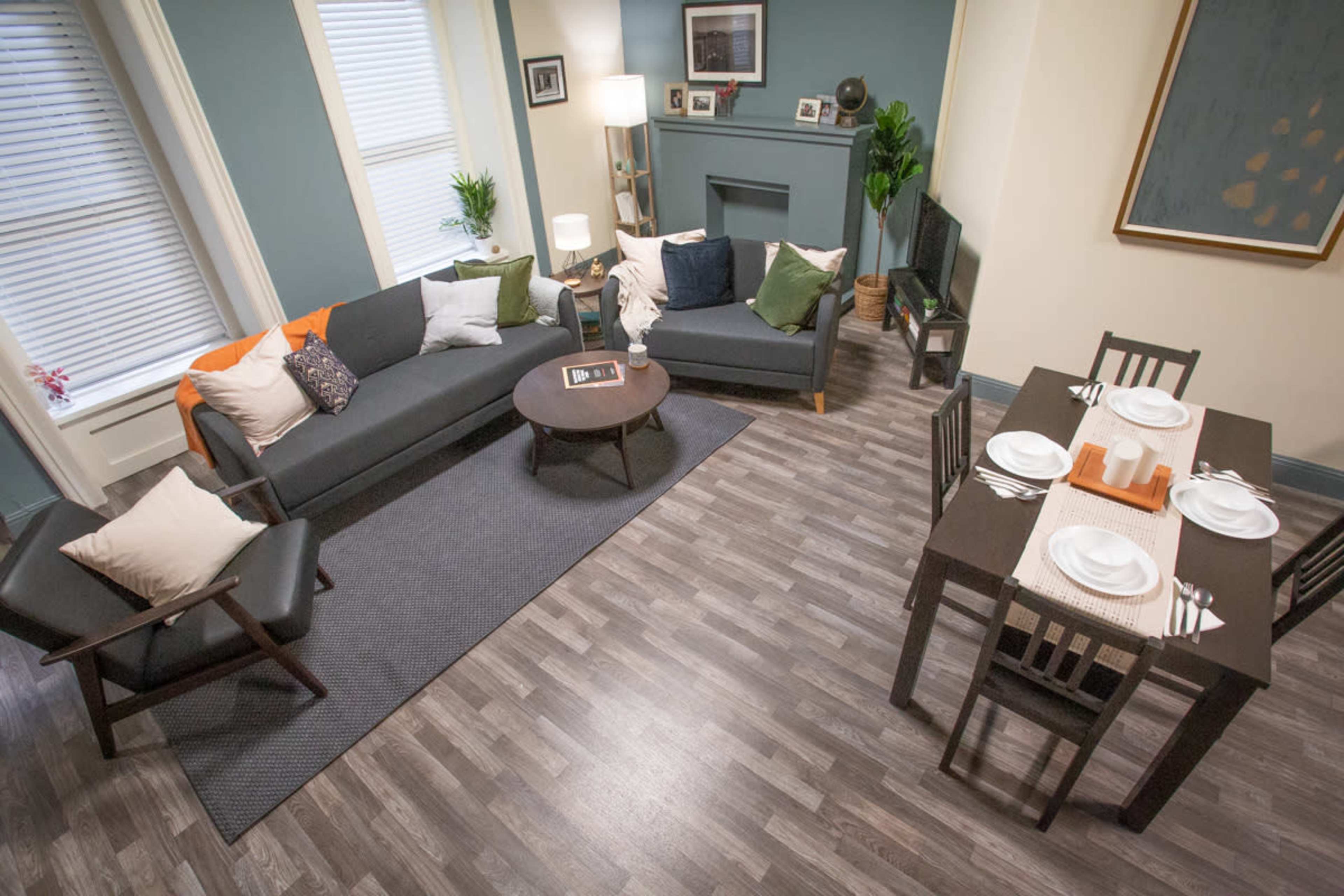 A decorated living room with a sofa, armchair, coffee table, and a dining table set for a meal, all situated on laminate flooring.