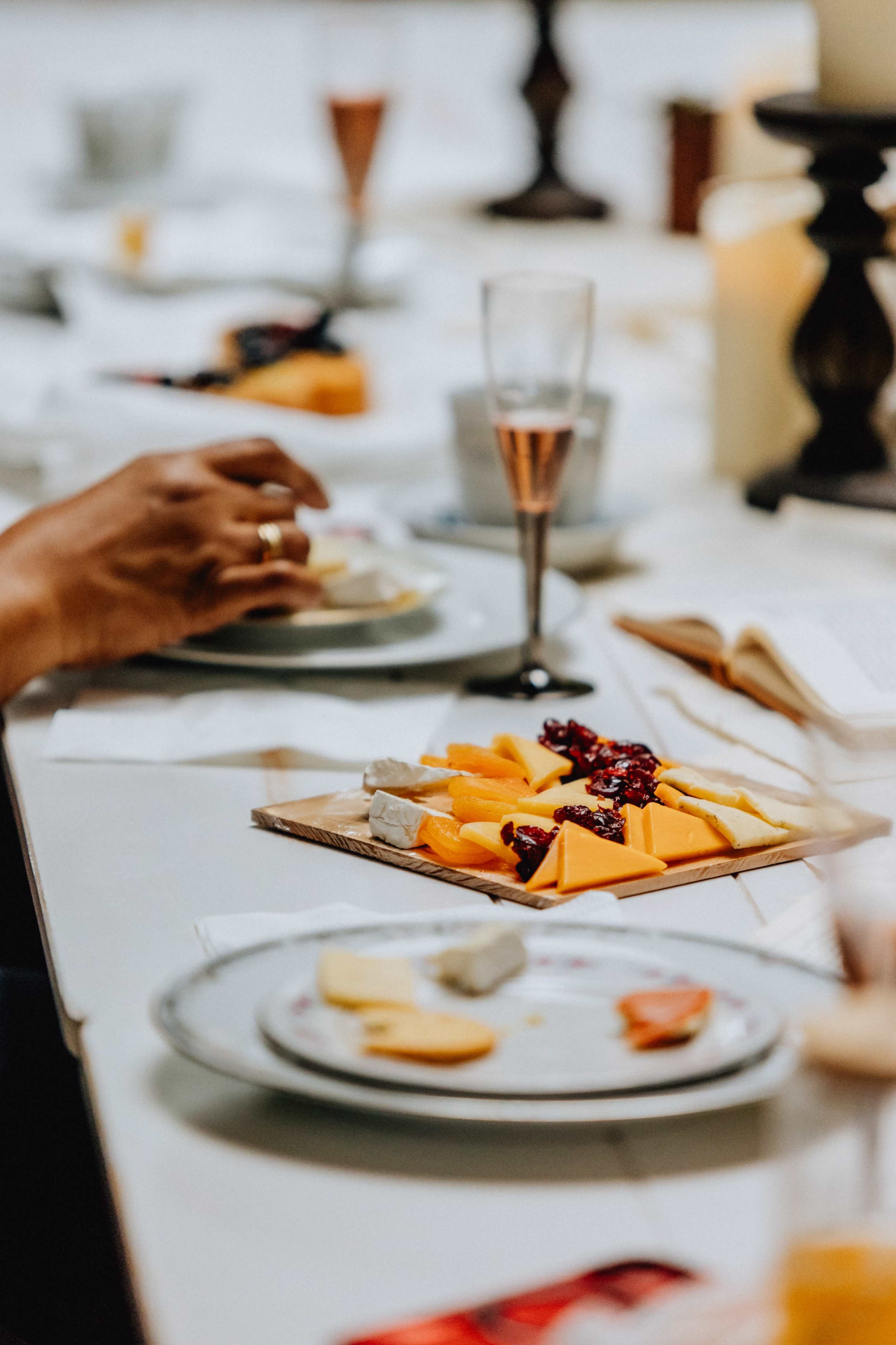 A table is set with plates of cheese, crackers, and drinks, while a hand reaches for food.