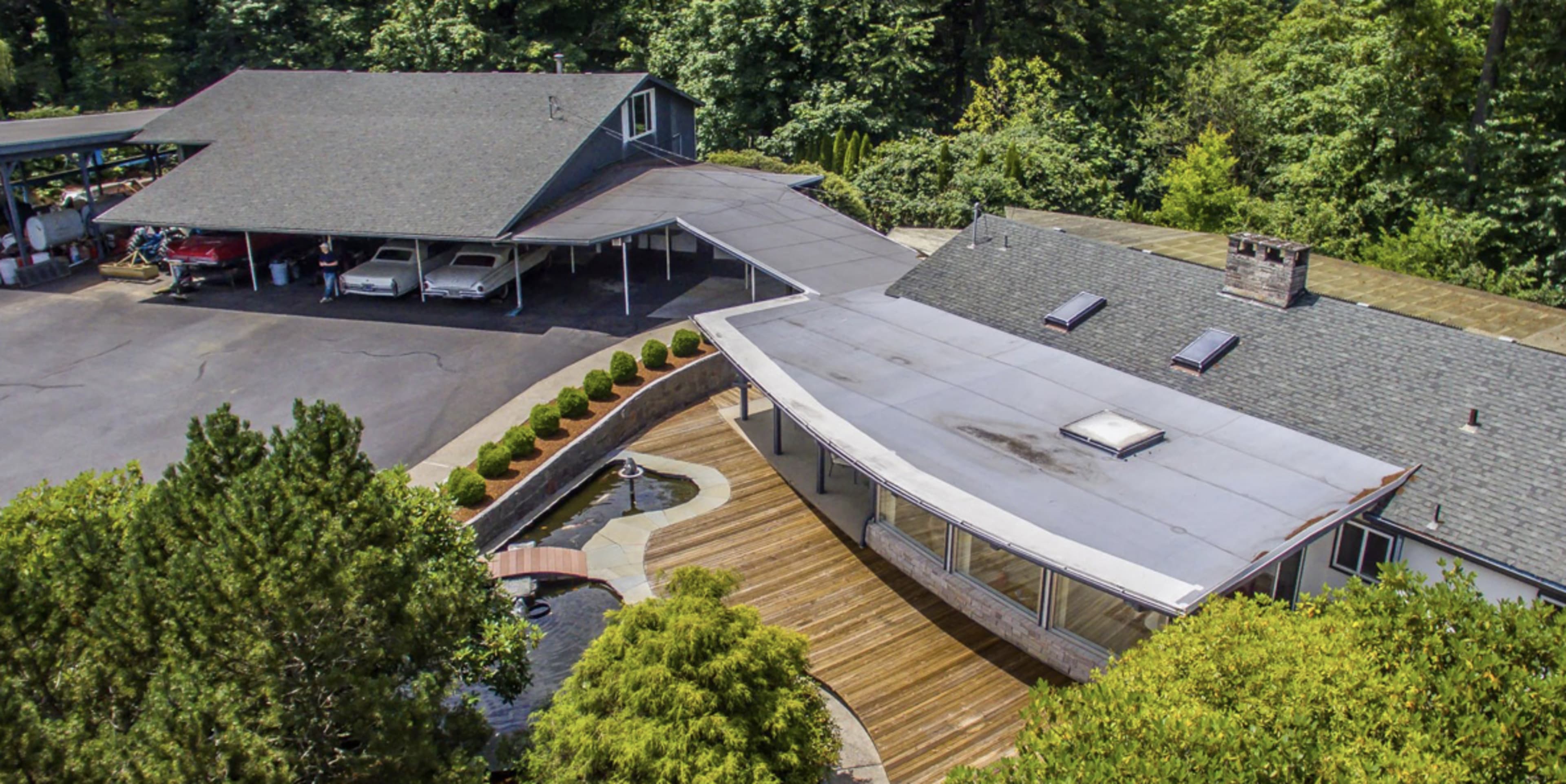 An aerial view of a modern house with a large deck, carport, and landscaped surroundings.