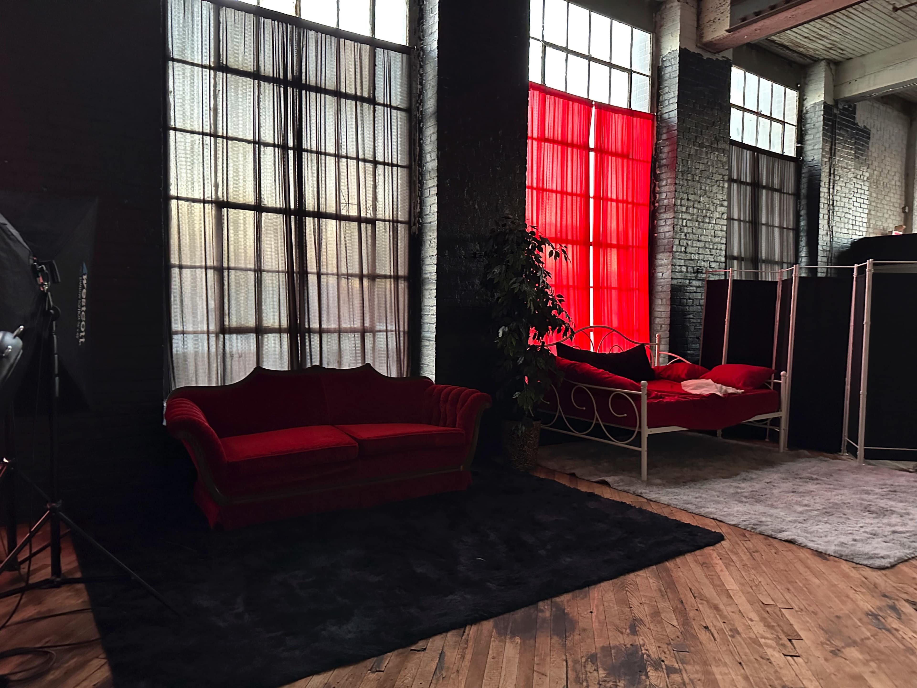 A spacious interior with large windows, featuring a red velvet couch and a white bed against a backdrop of black and red curtains.