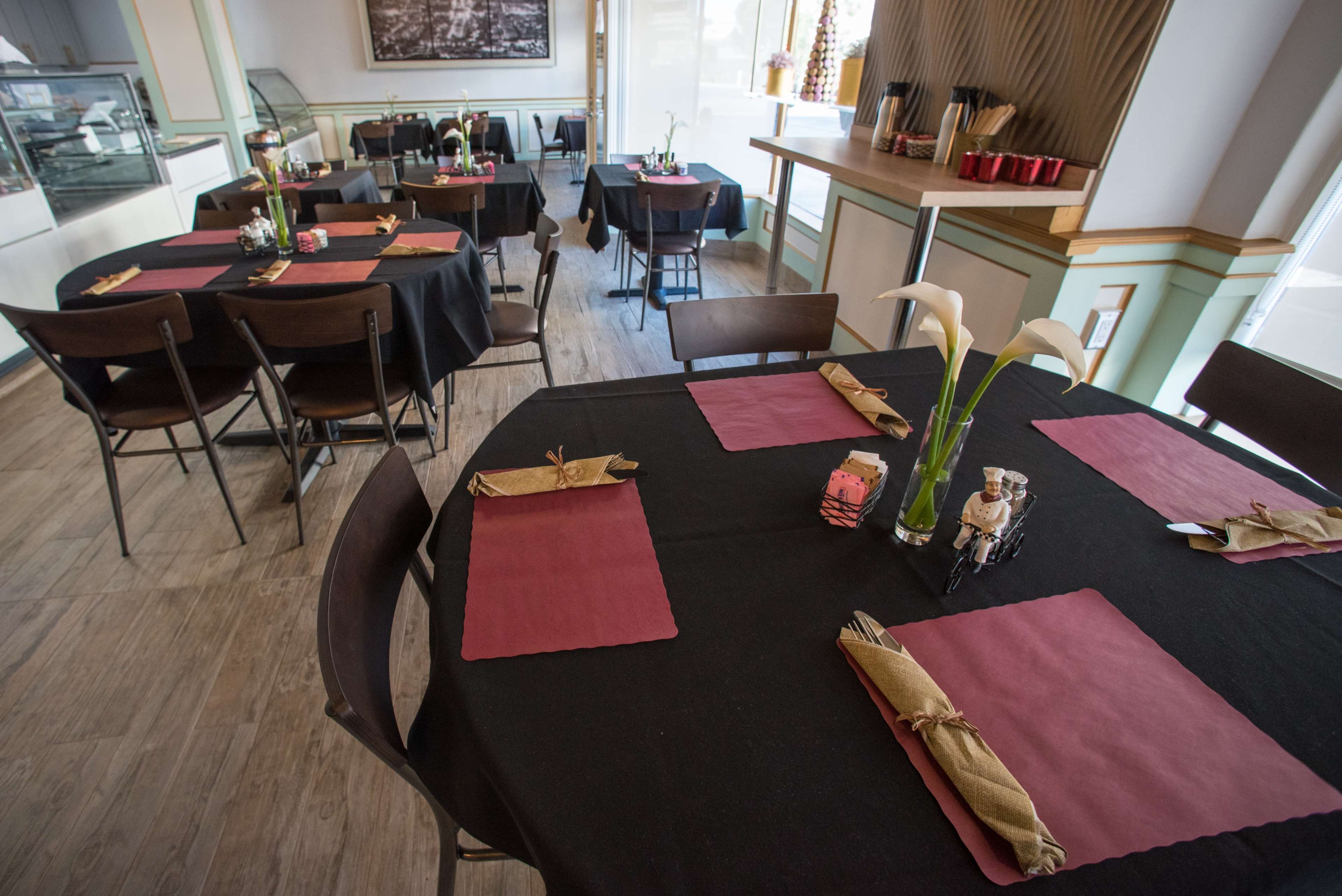 A dining area with black tables covered by dark cloths and adorned with maroon placemats, each set with utensils and decorative centerpieces.