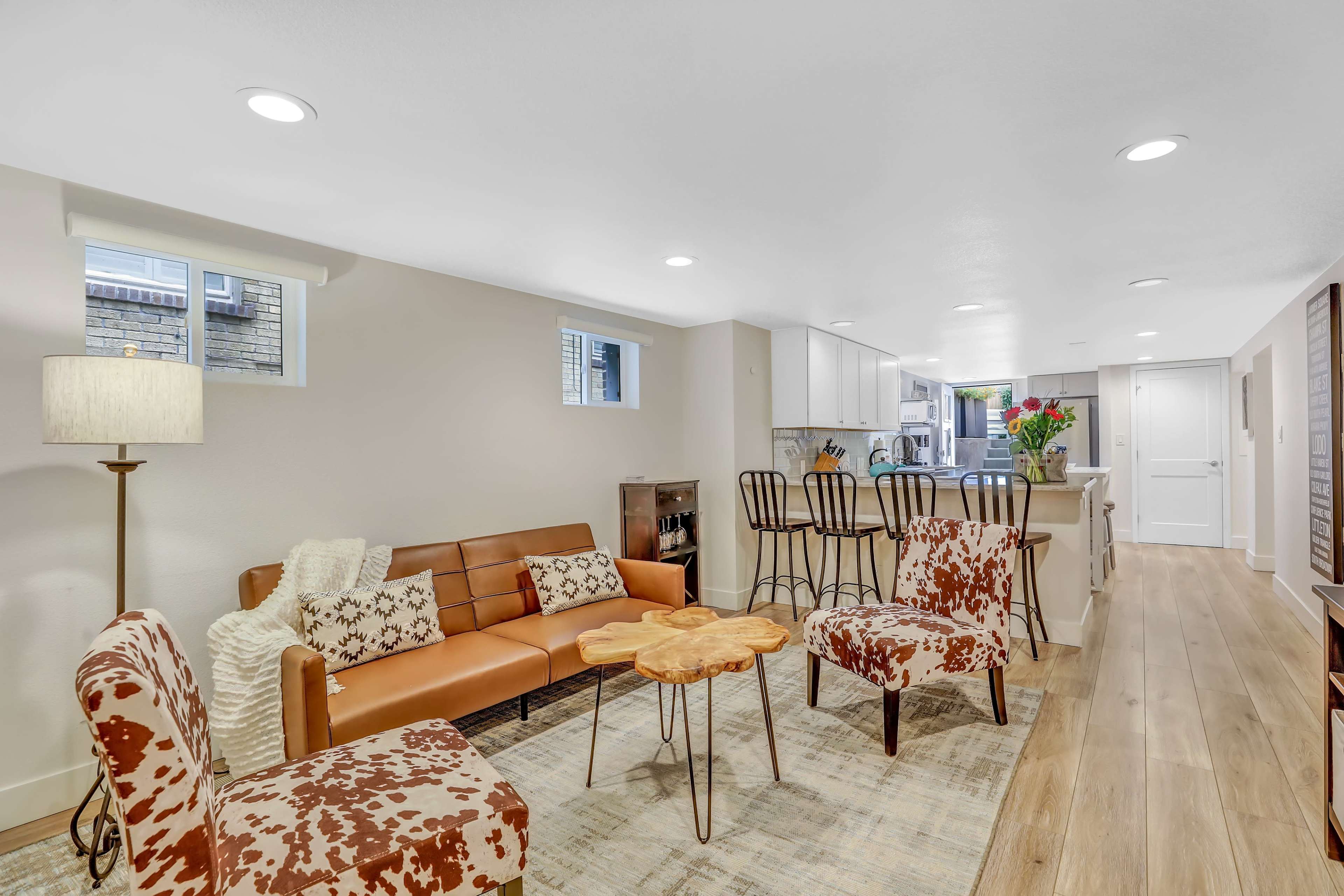 The image shows a modern living room with brown leather furniture, a wooden coffee table, and a kitchen in the background.