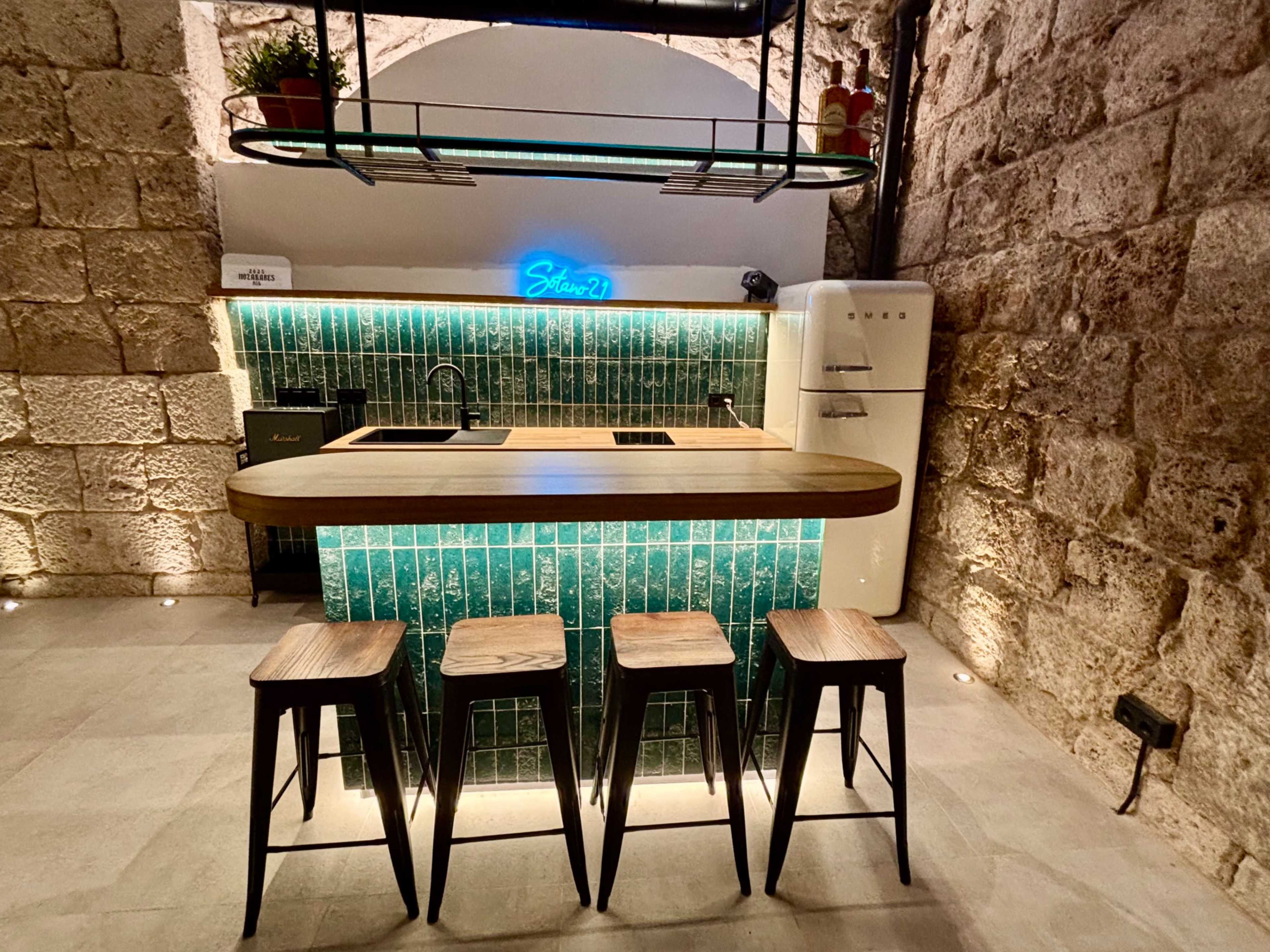 The image showcases a modern kitchen with a teal tile backsplash, a wooden countertop, and four black bar stools positioned in front of it.