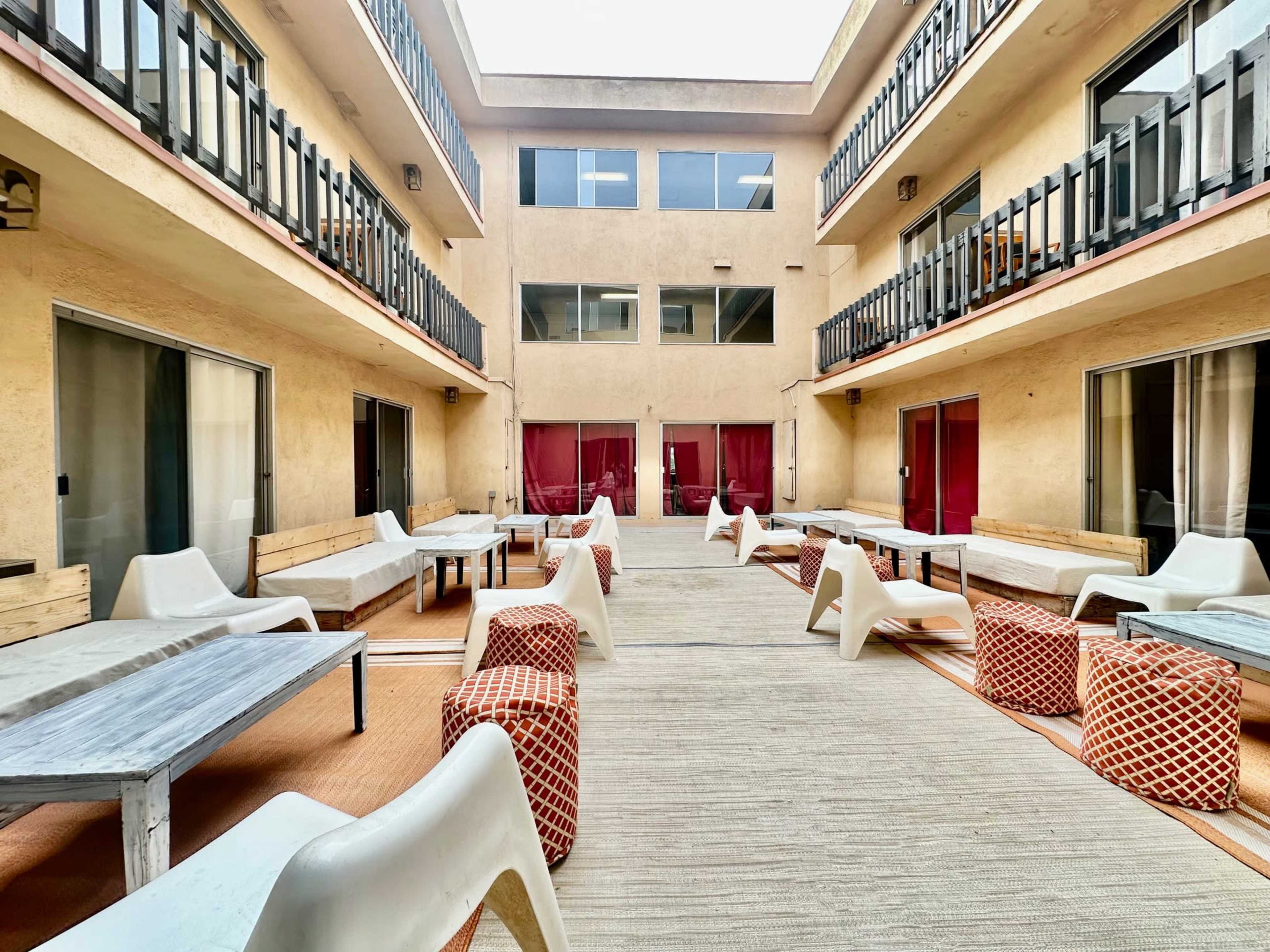 The image shows a spacious courtyard area of a two-story building with multiple seating arrangements and large windows facing inward.