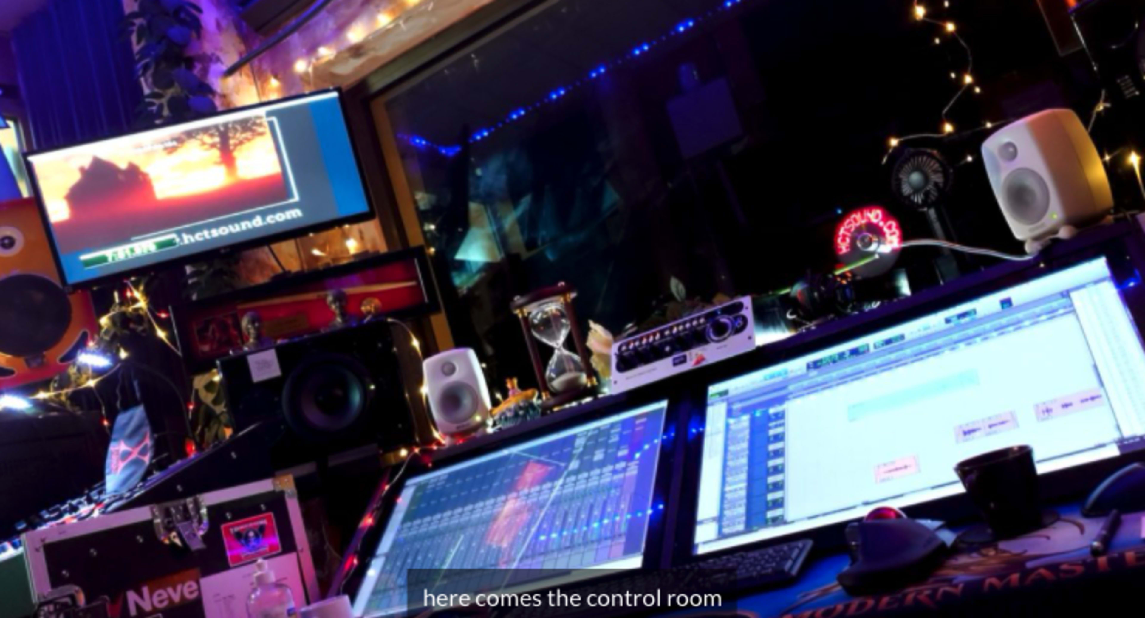A music control room equipped with digital mixing consoles, speakers, and illuminated screens.