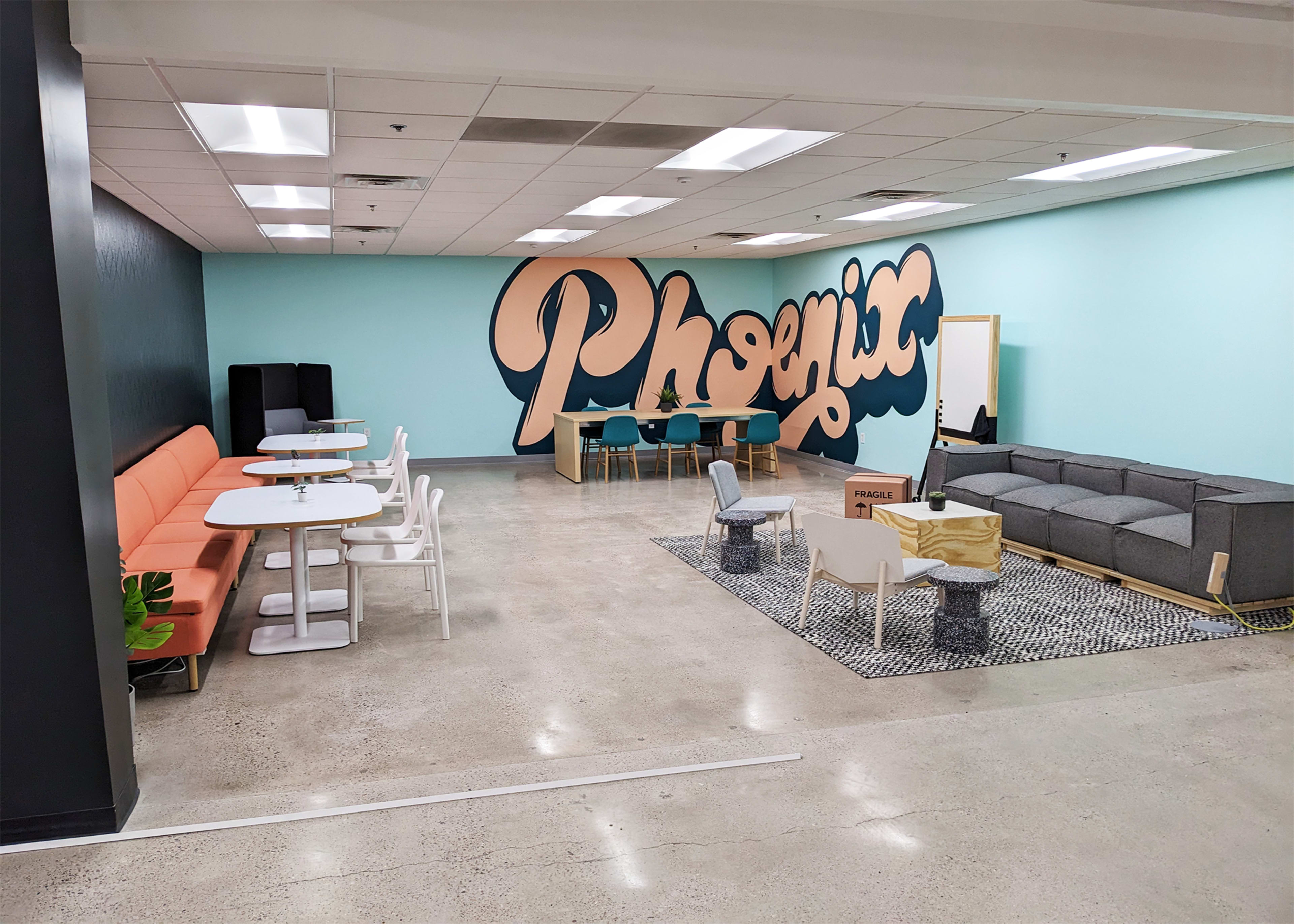 A modern lounge area with colorful seating, tables, and a large mural featuring the word "Phoenix" on the wall.