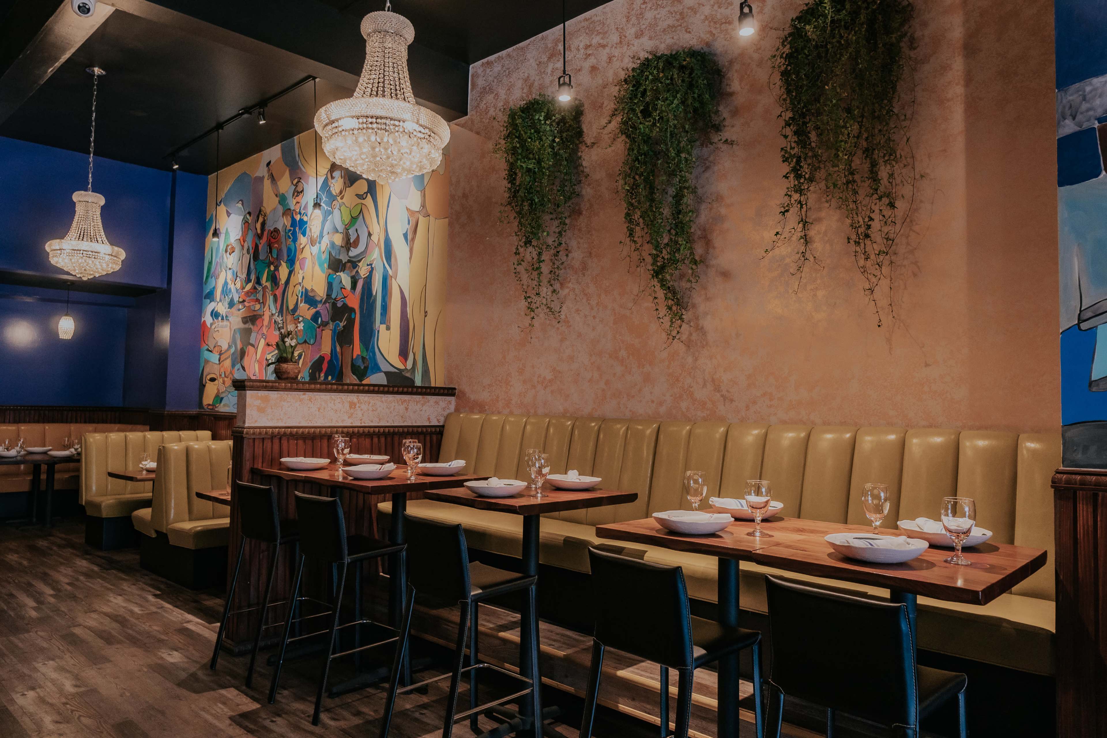 The image shows a modern restaurant interior featuring a yellow upholstered seating area, wooden tables, and a colorful mural on the wall.
