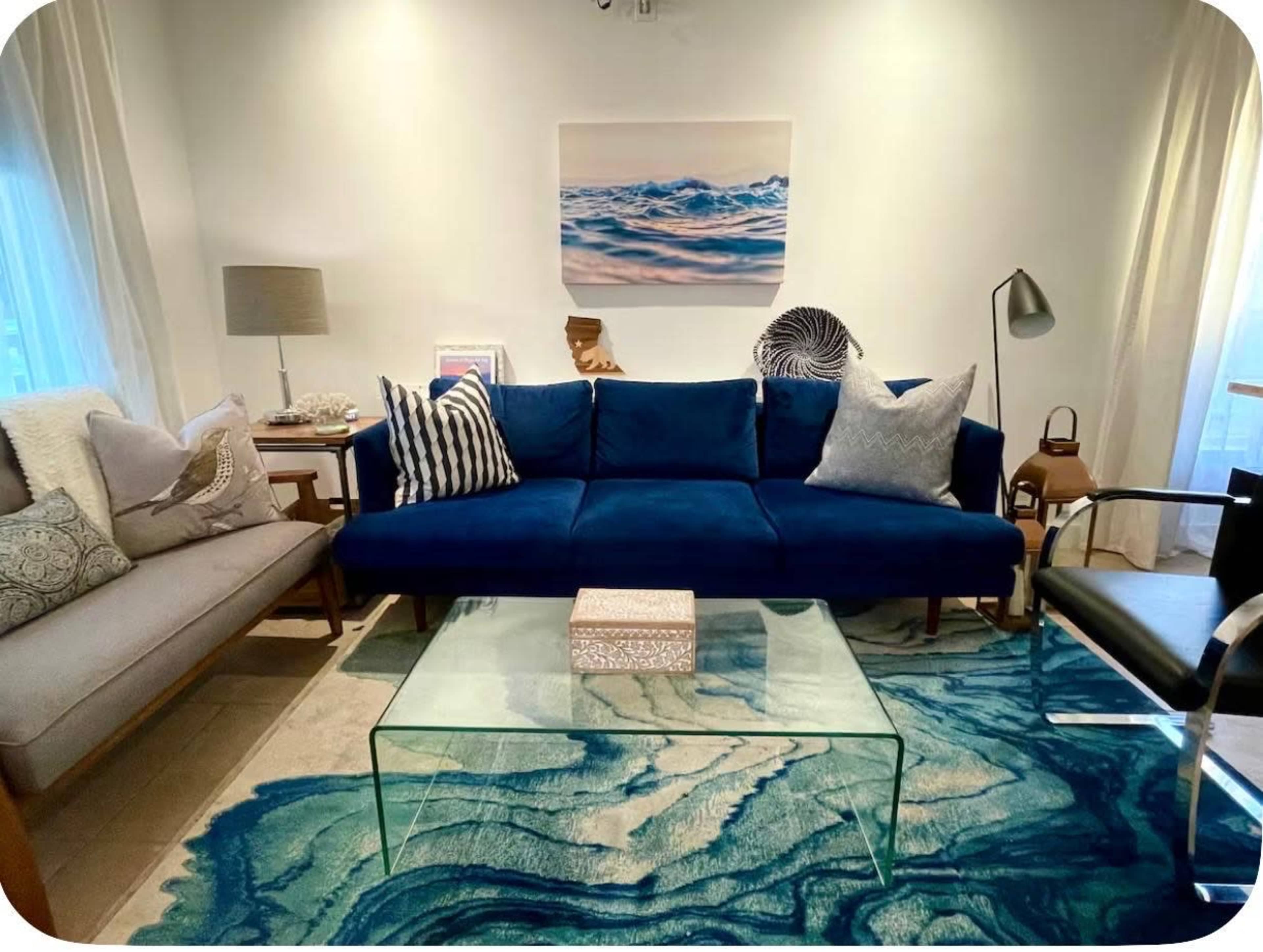 The image depicts a modern living room with a blue couch, a glass coffee table, and decorative elements like cushions and artwork.