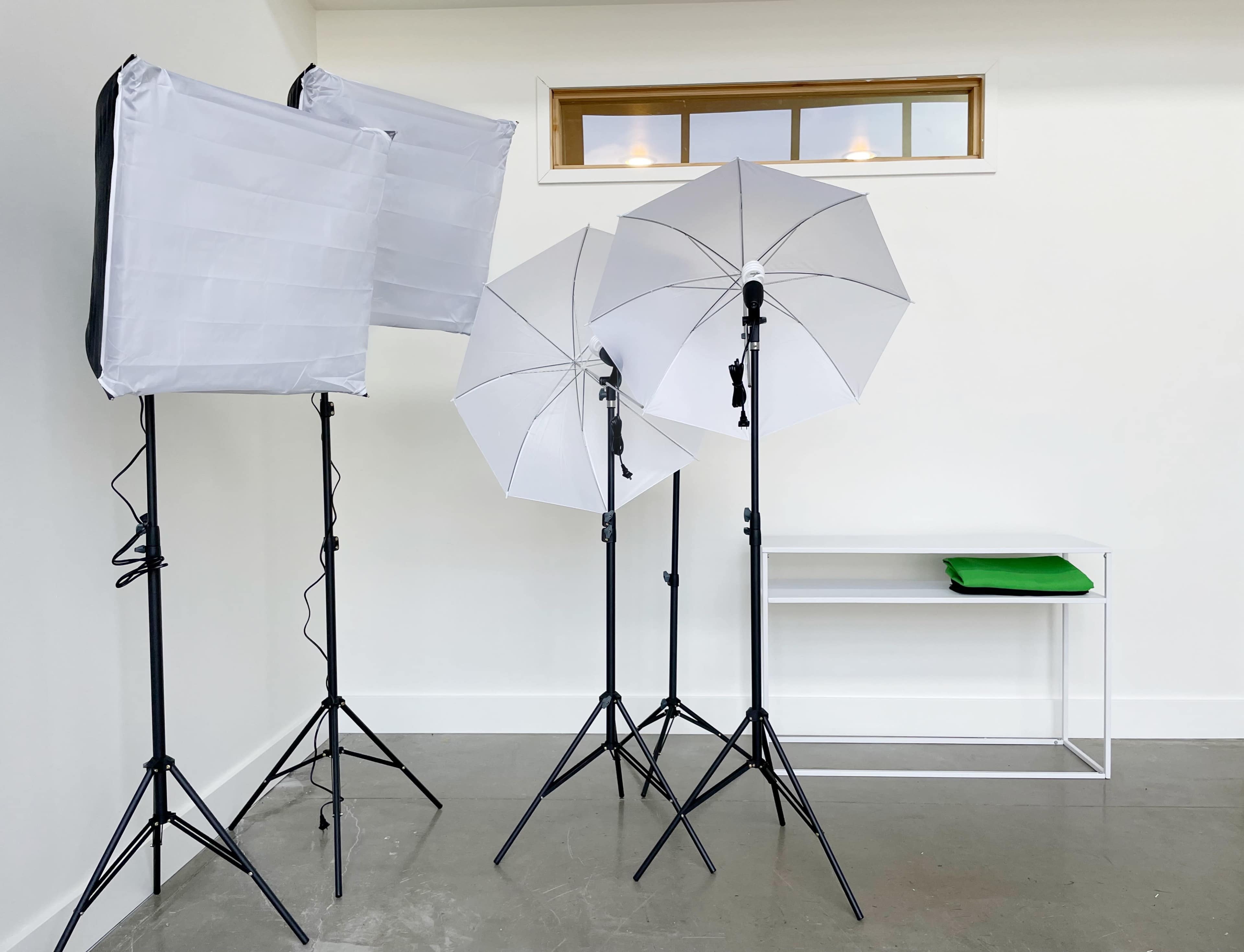 The image shows three light umbrellas and a white table set against a plain wall.