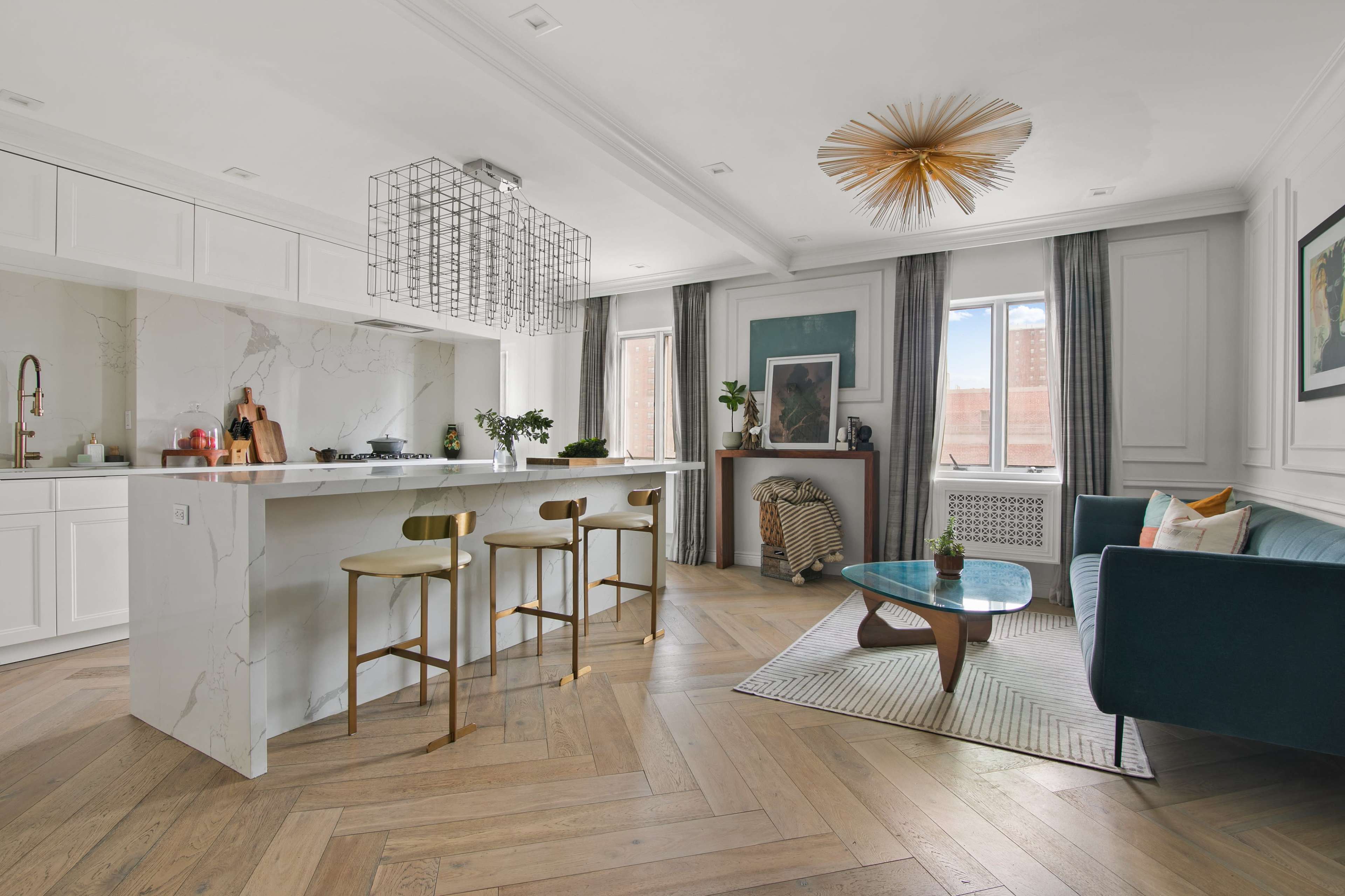 The image depicts a modern kitchen and living area featuring a central island with bar stools, a large window with soft light, and contemporary furniture arranged in an open layout.
