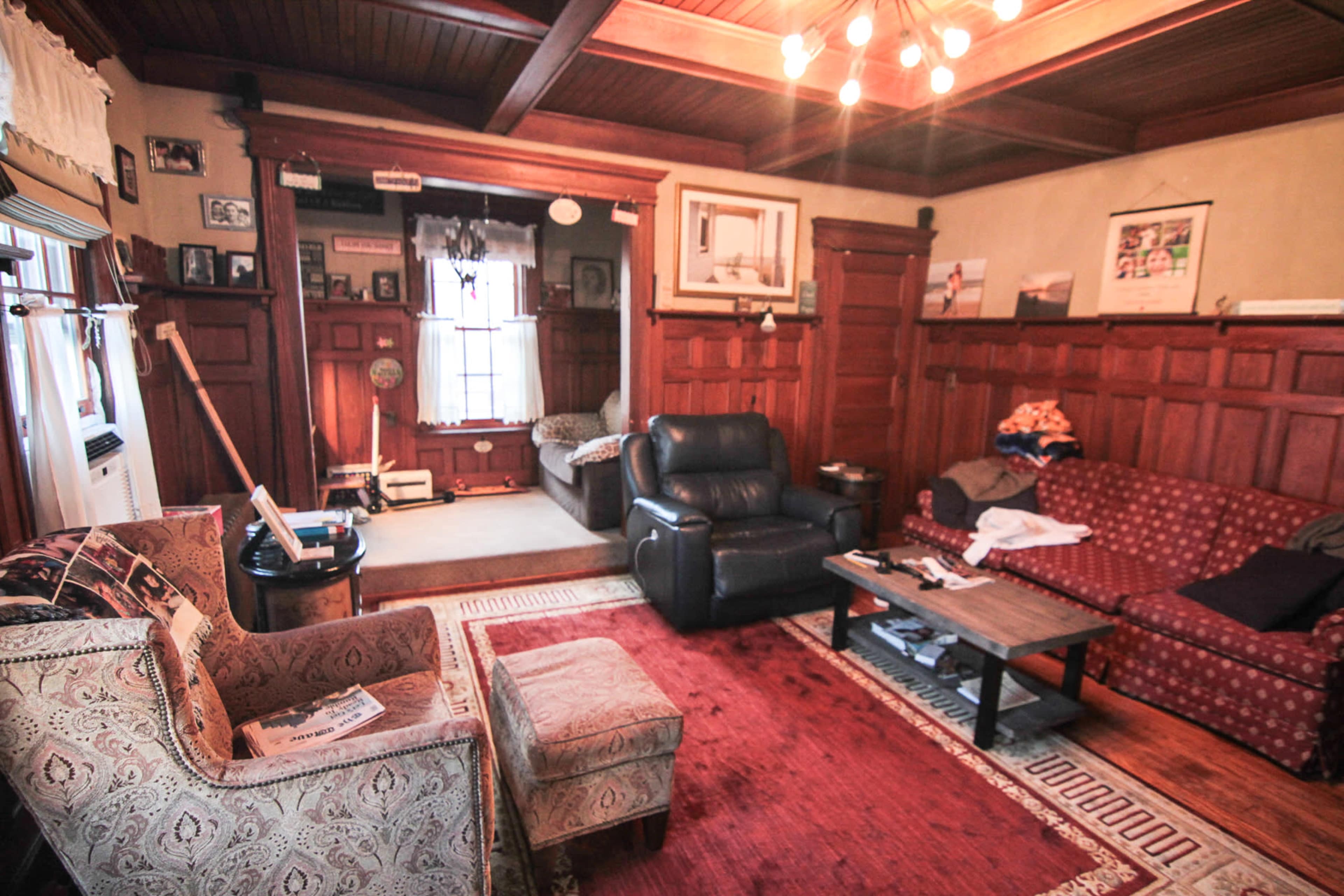 A living room with wooden paneling, two sofas, a coffee table, and various framed pictures on the walls.
