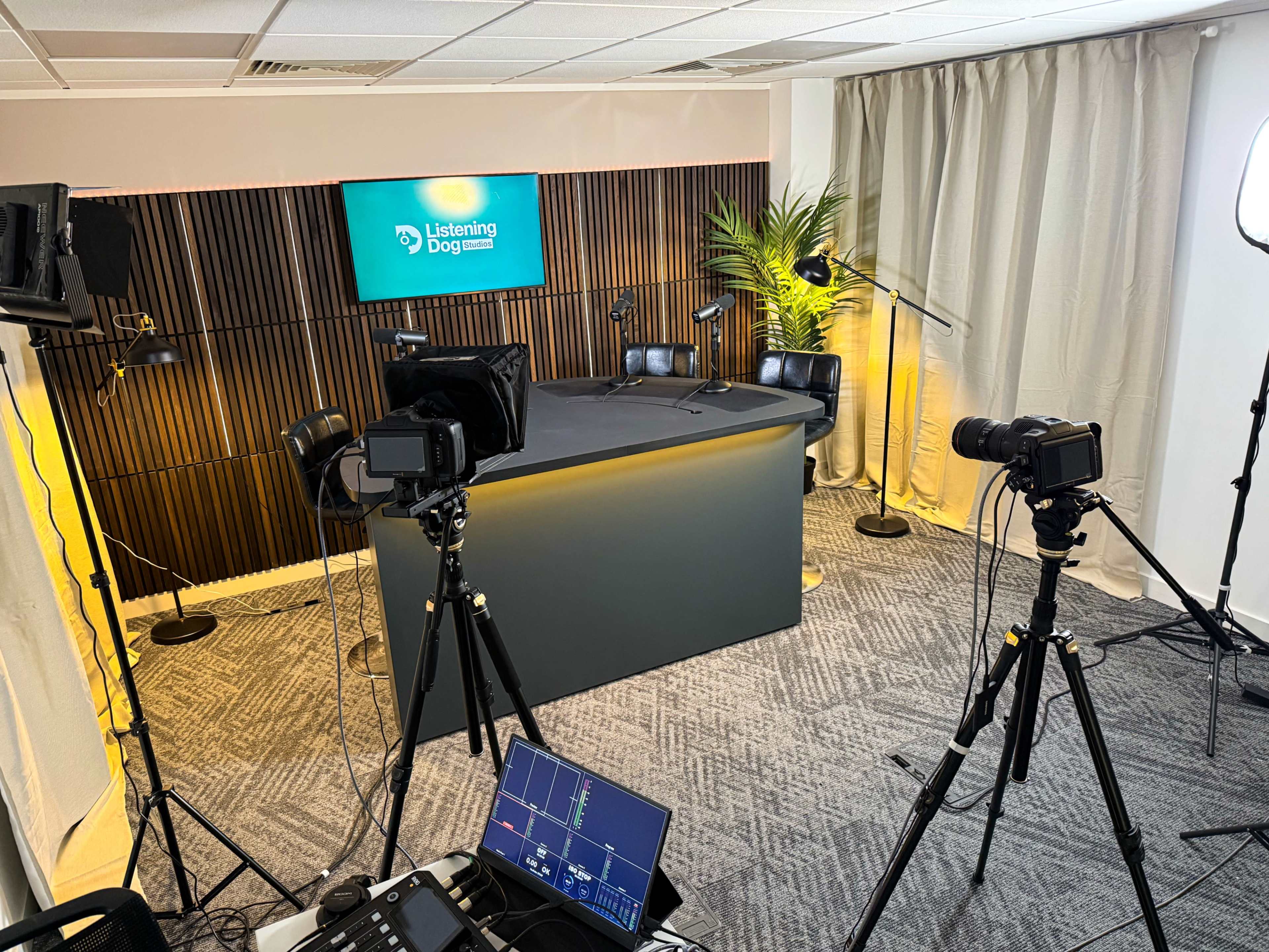 The image shows a modern studio setup for a podcast or video recording, featuring a central table, cameras on tripods, and professional lighting equipment.