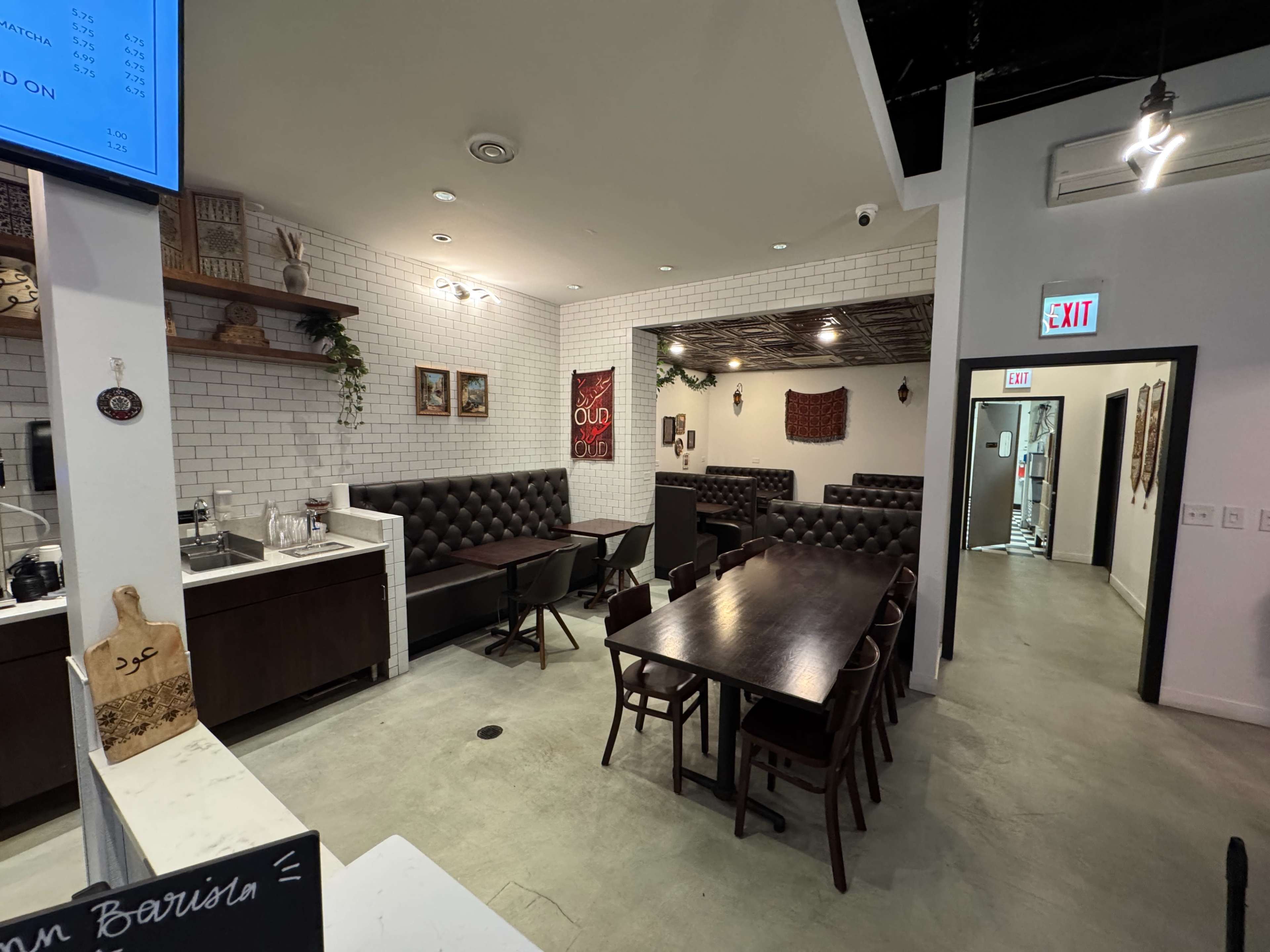 The image shows a modern restaurant interior with a mix of booth seating and wooden tables arranged in a spacious layout.