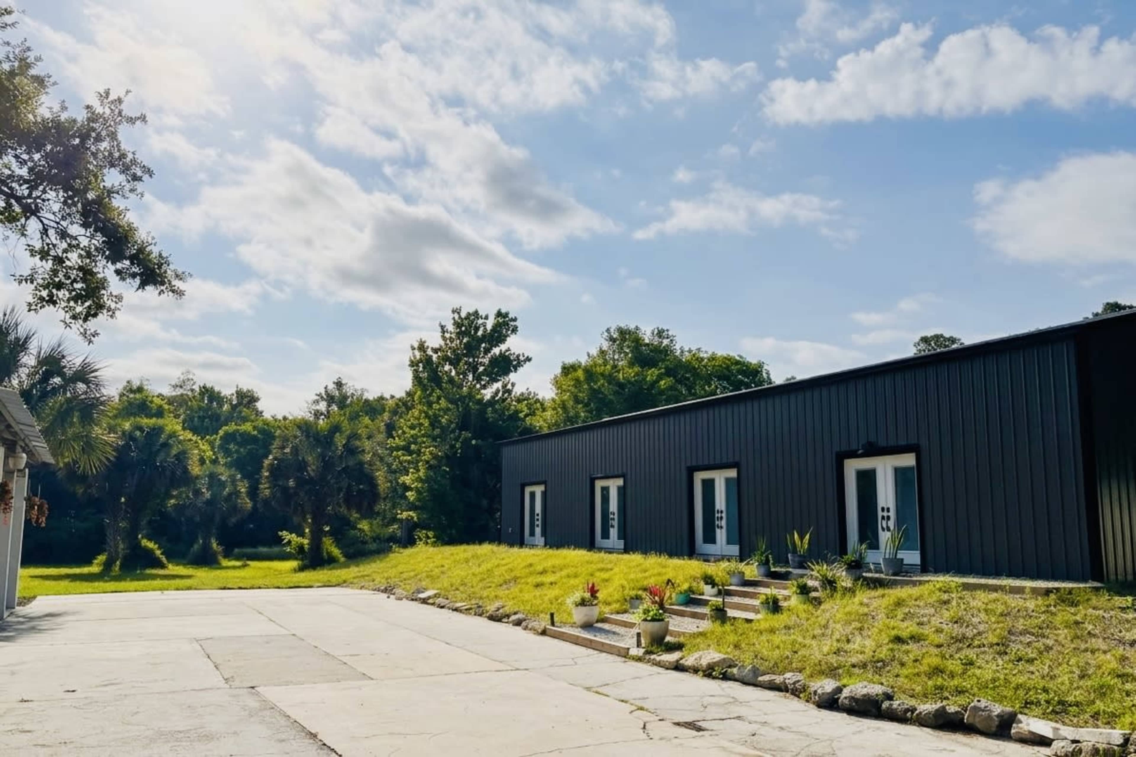 A modern building with a black exterior is situated beside a grassy area and surrounded by trees under a partly cloudy sky.
