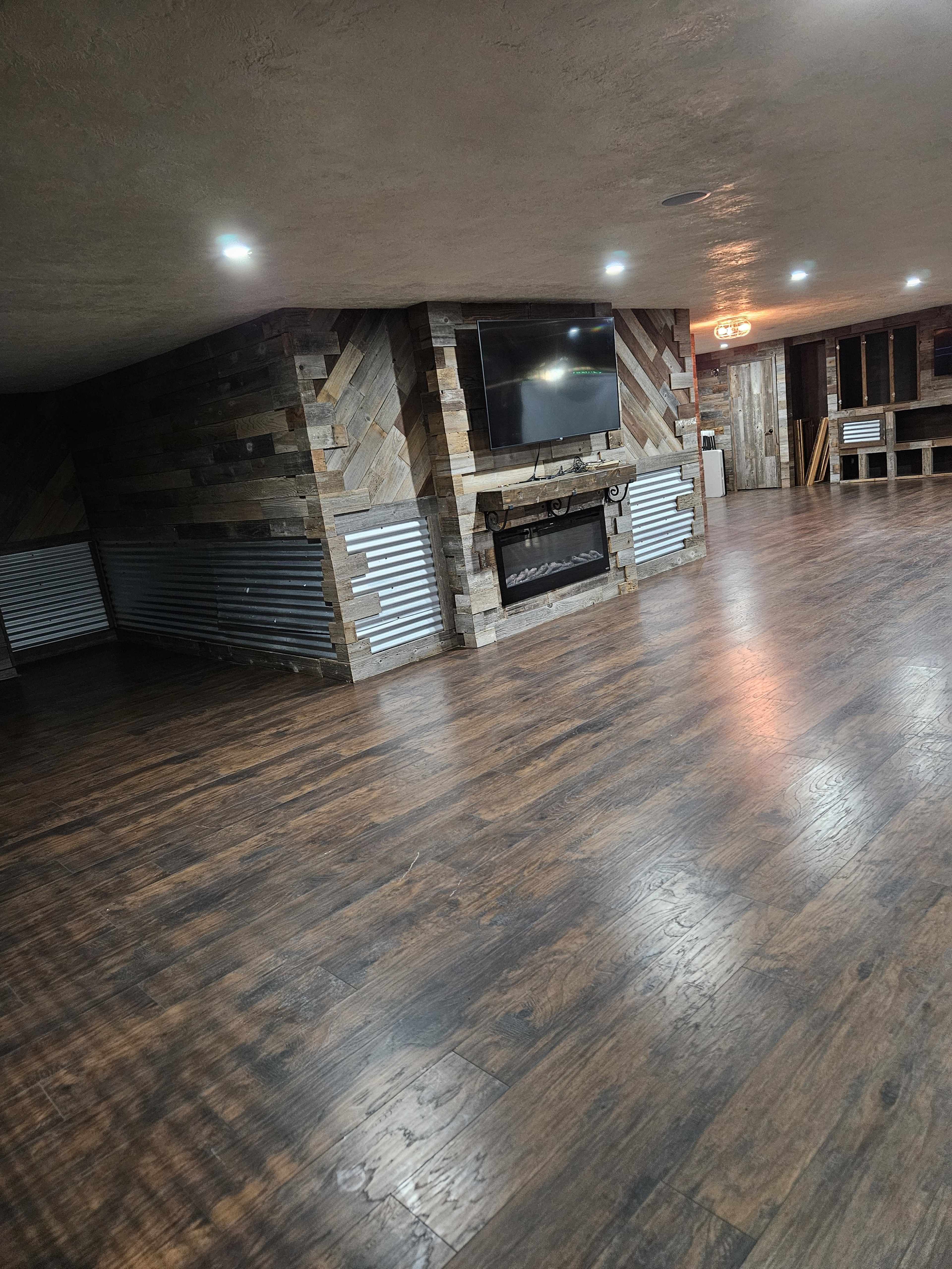 The image shows a spacious interior room with wooden flooring, a stone feature wall with a television, and a fireplace.