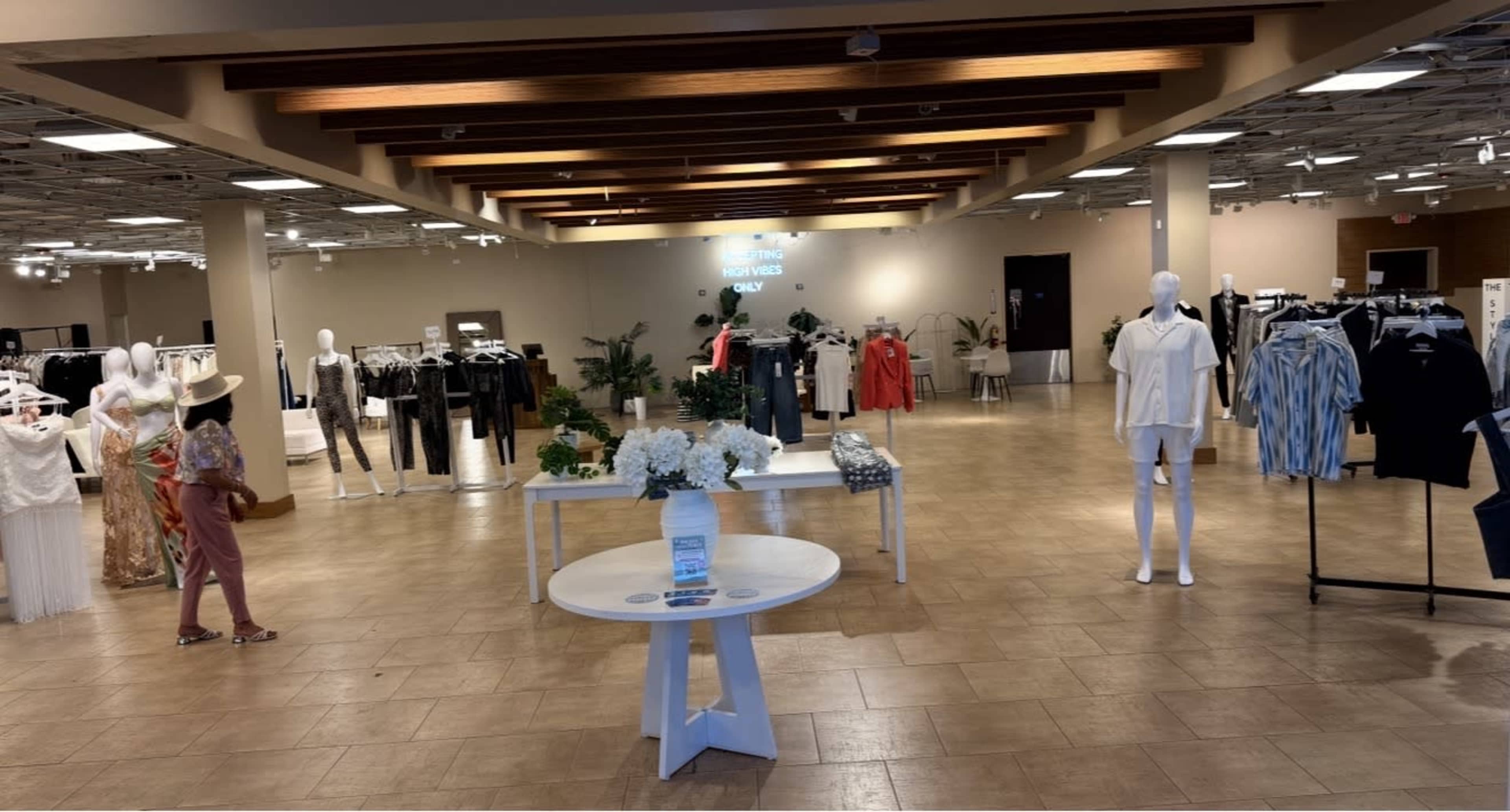 The interior of a clothing store features clothing displays on mannequins and racks, arranged in a spacious layout with neutral-colored walls and lighting.