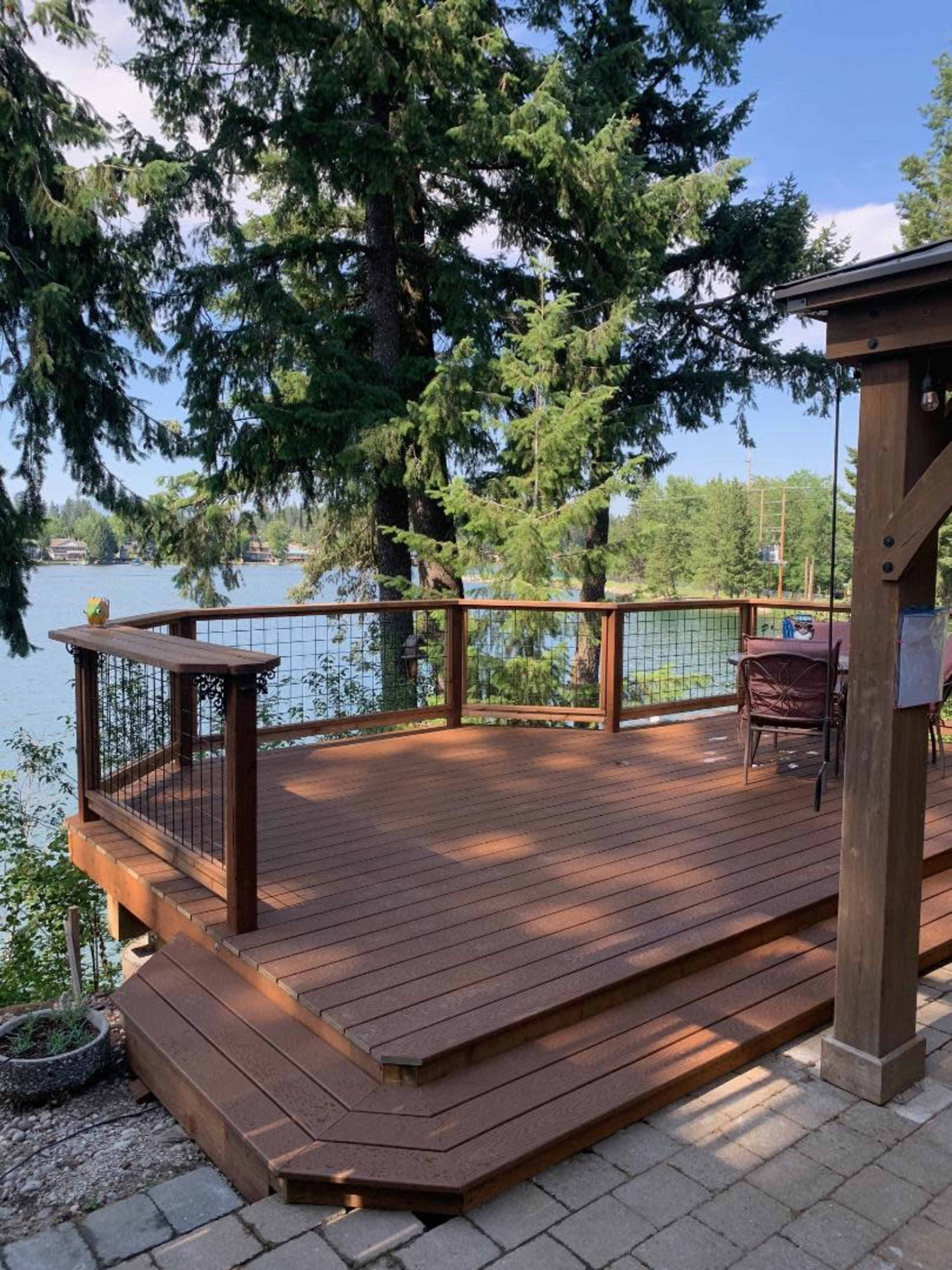 A wooden deck with railings, surrounded by tall trees, leading down to a body of water.