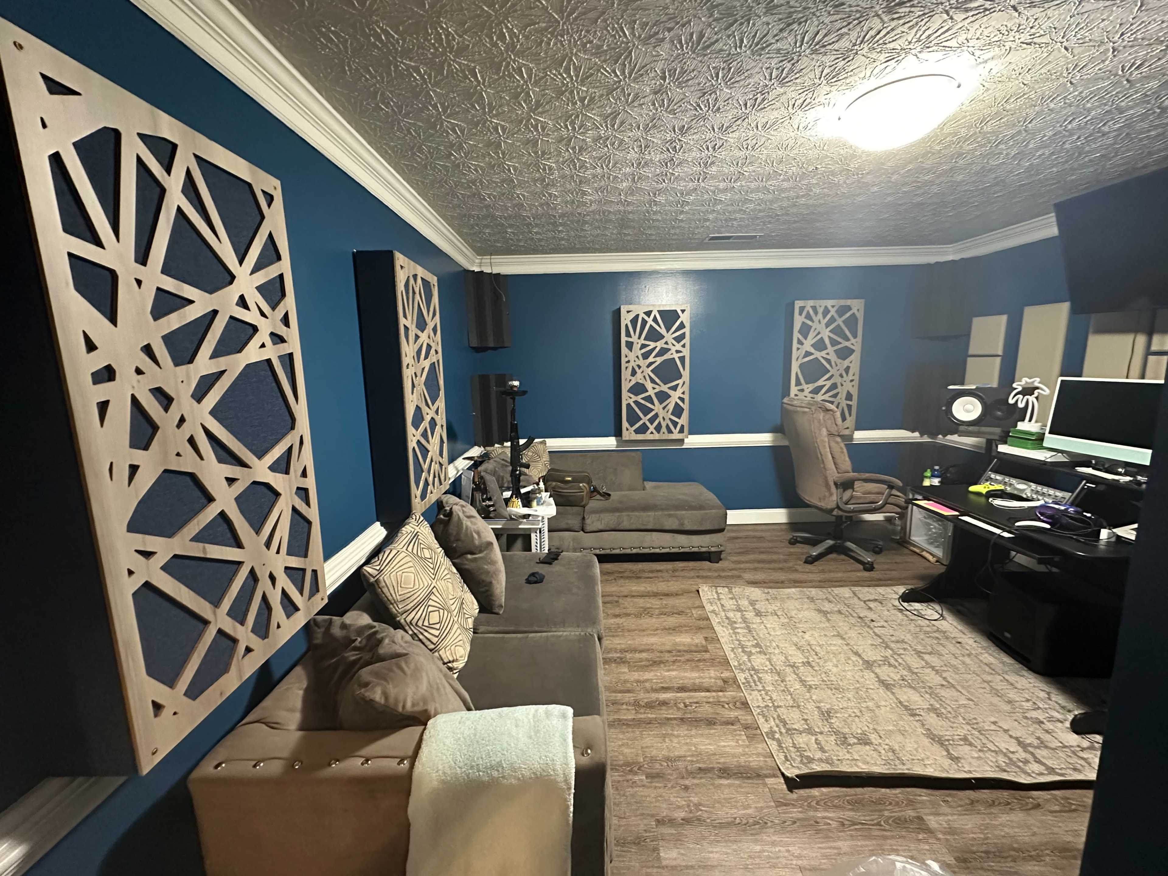 A room with blue walls, decorative wooden panels, a large rug, a seating area with two couches, and a workspace featuring a computer desk and monitors.