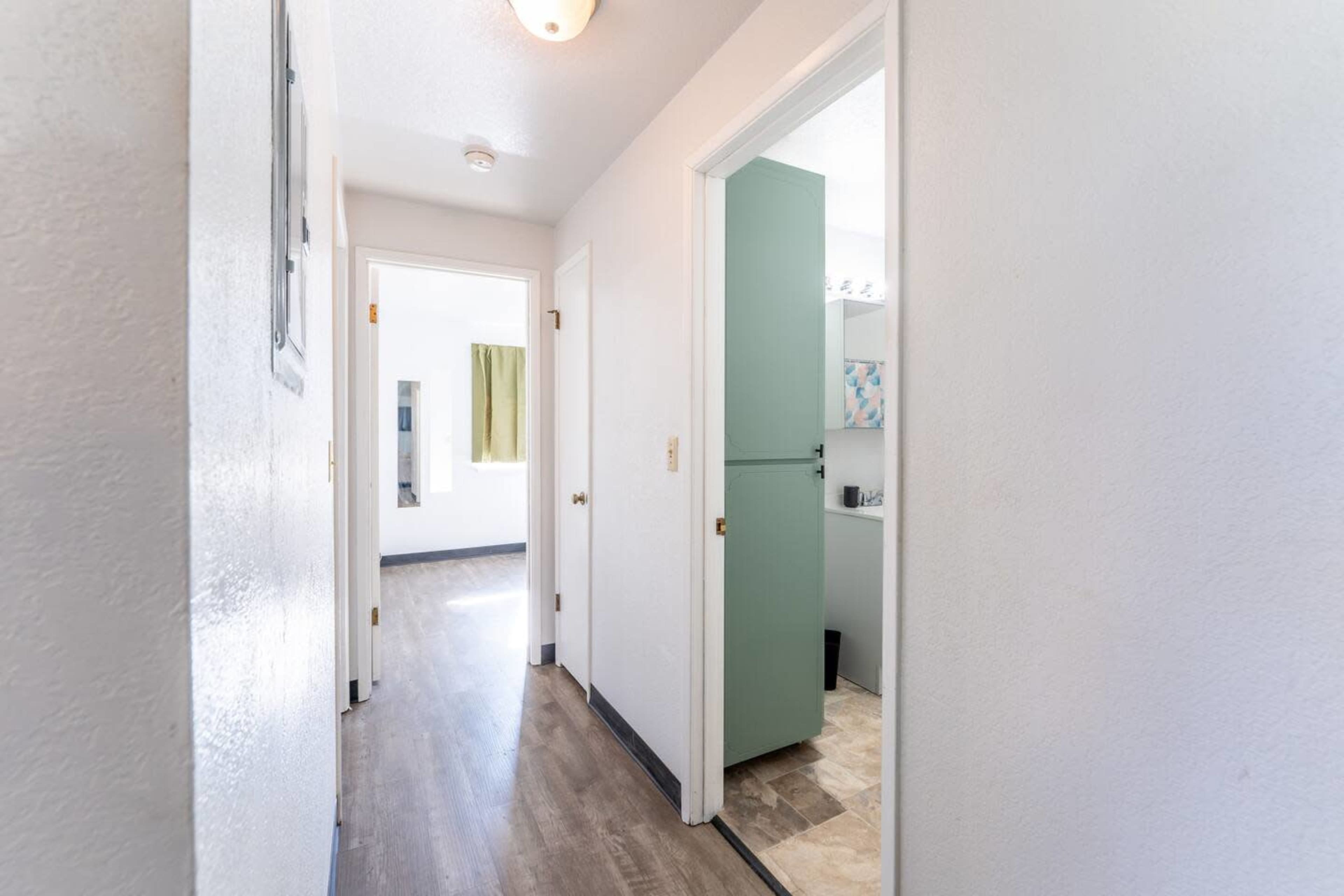 A narrow hallway with white walls, light-colored flooring, and a door leading to a room on the right.