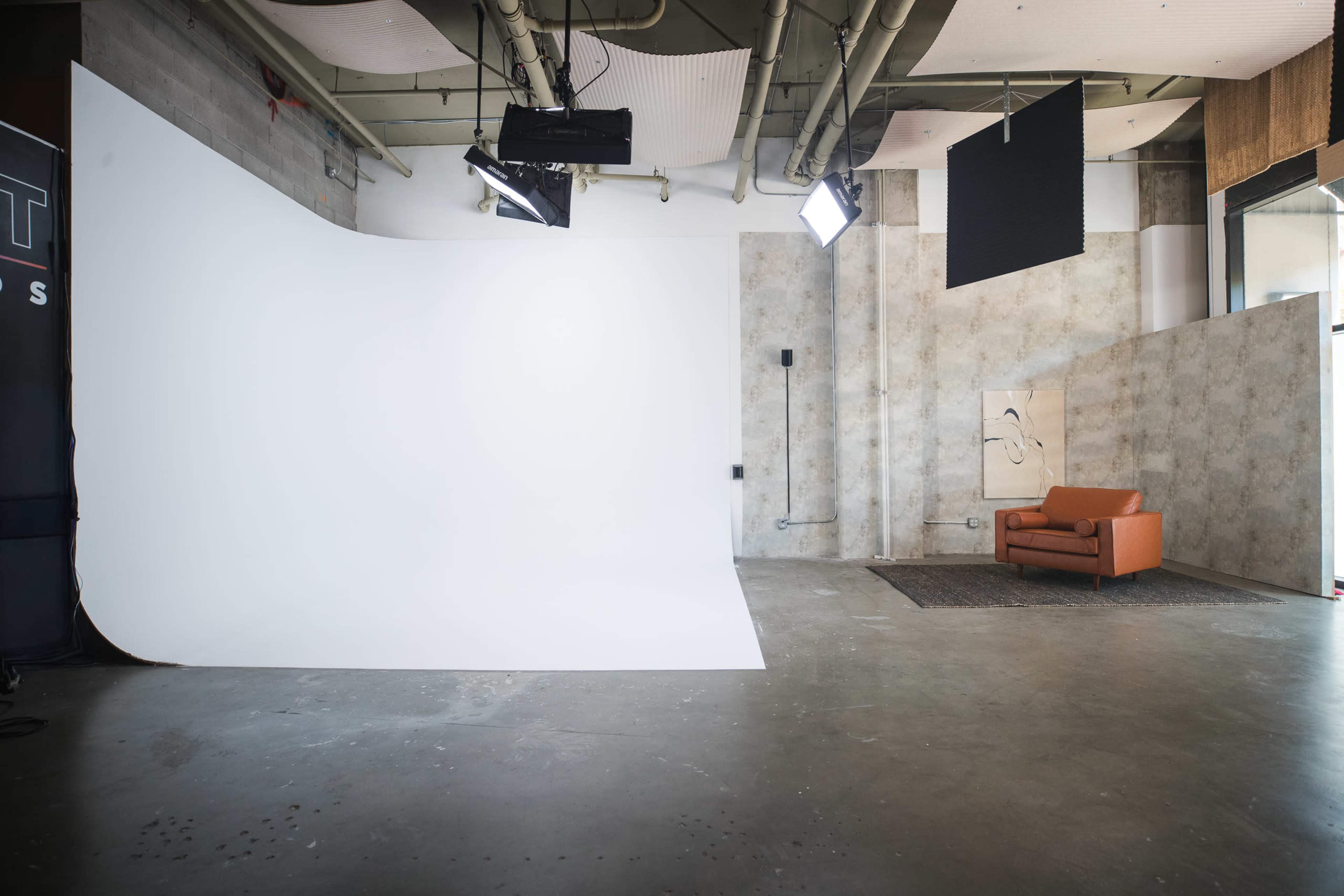 The image shows a spacious studio with a white backdrop, a brown sofa, and various studio lights.
