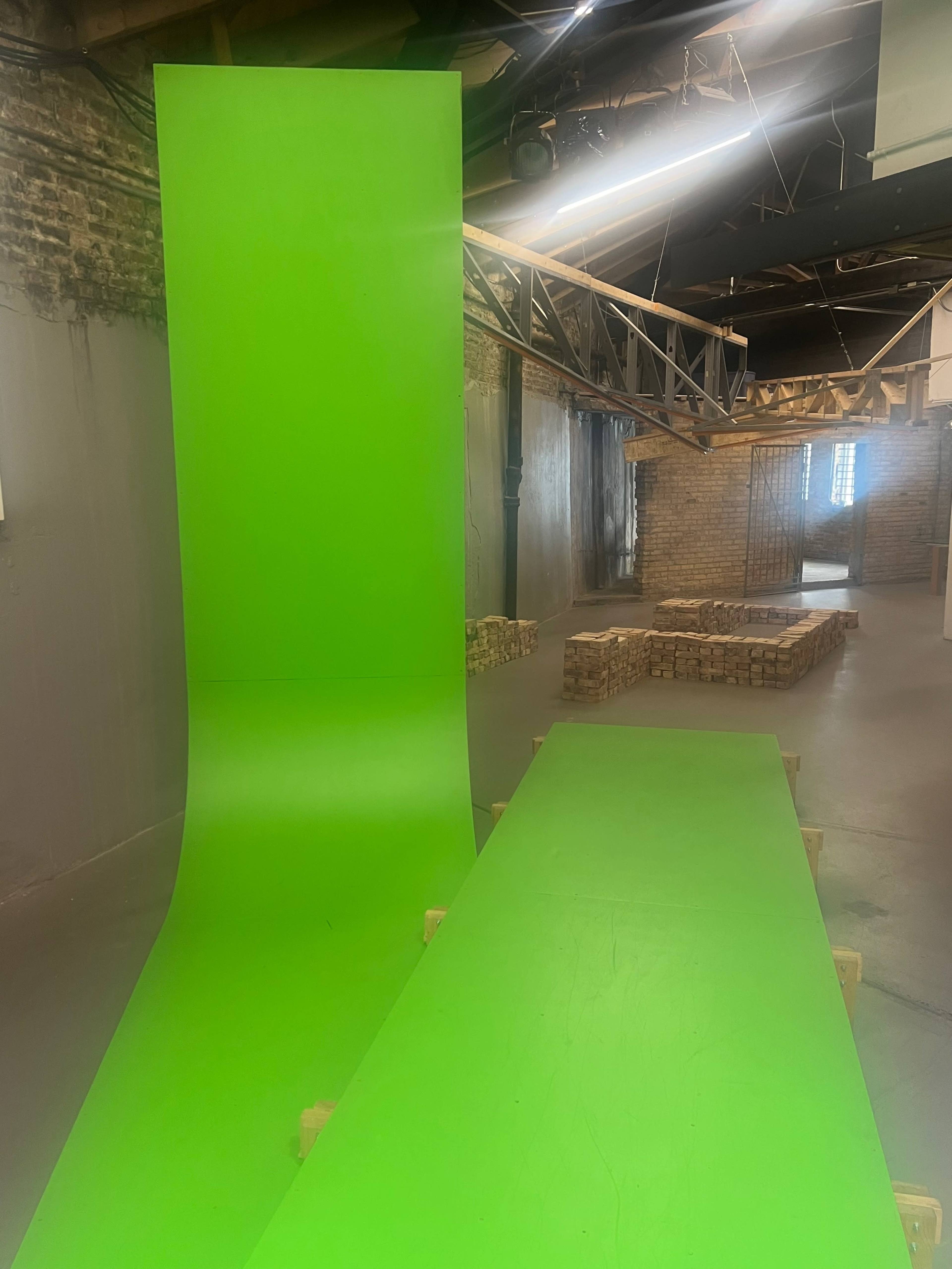 The image shows a spacious interior with a bright green backdrop and flooring, arranged on wooden supports, within a brick-walled environment.