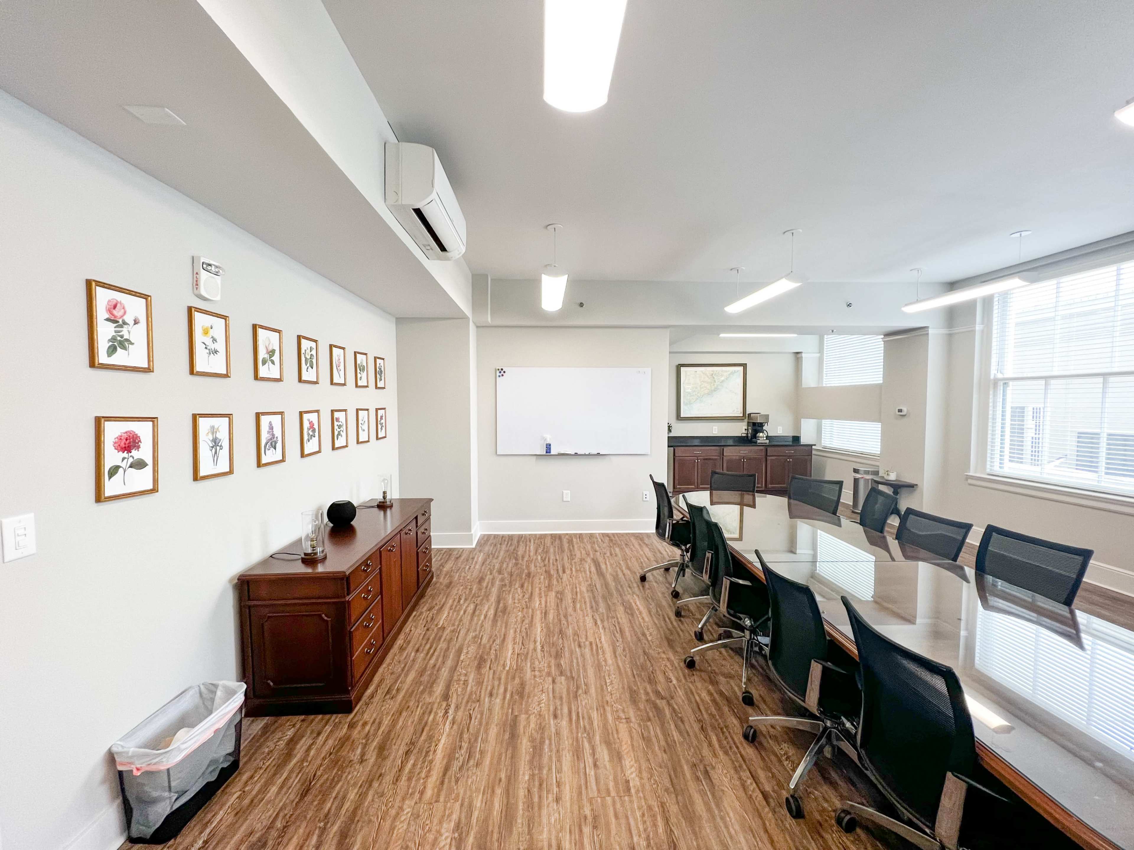 A conference room with a long table, black chairs, a whiteboard, and artwork displayed on the walls.