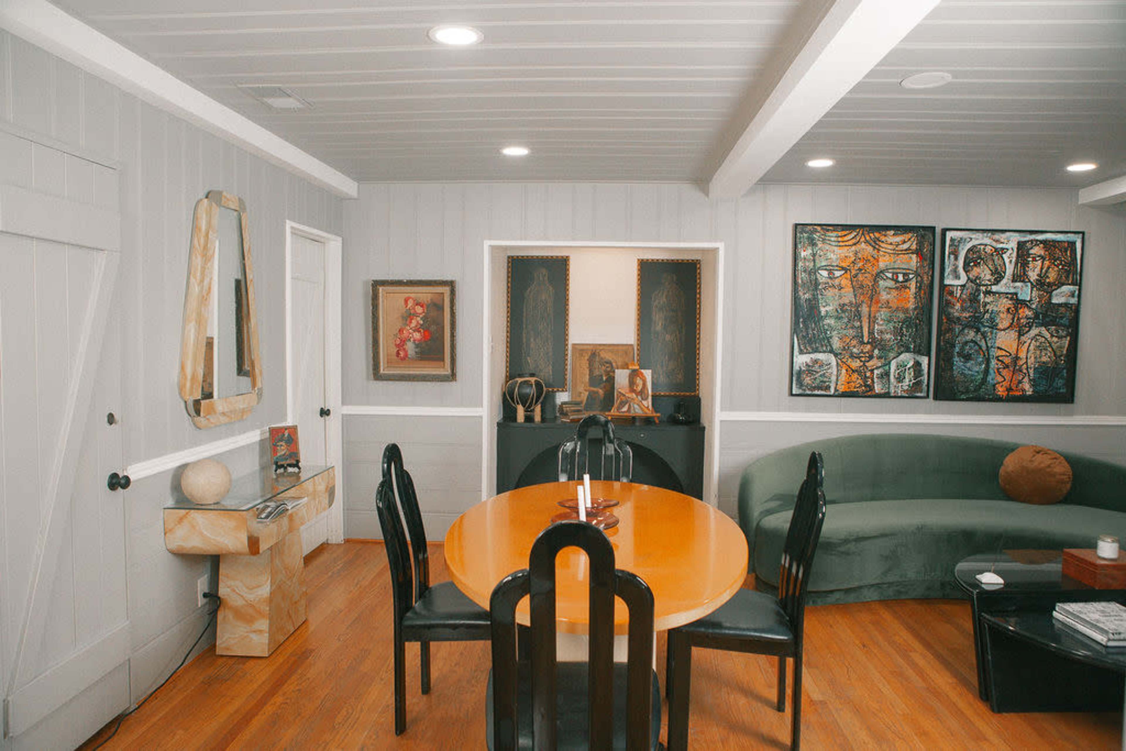 A modern living space featuring a round orange dining table, a green couch, and artwork displayed on the walls.