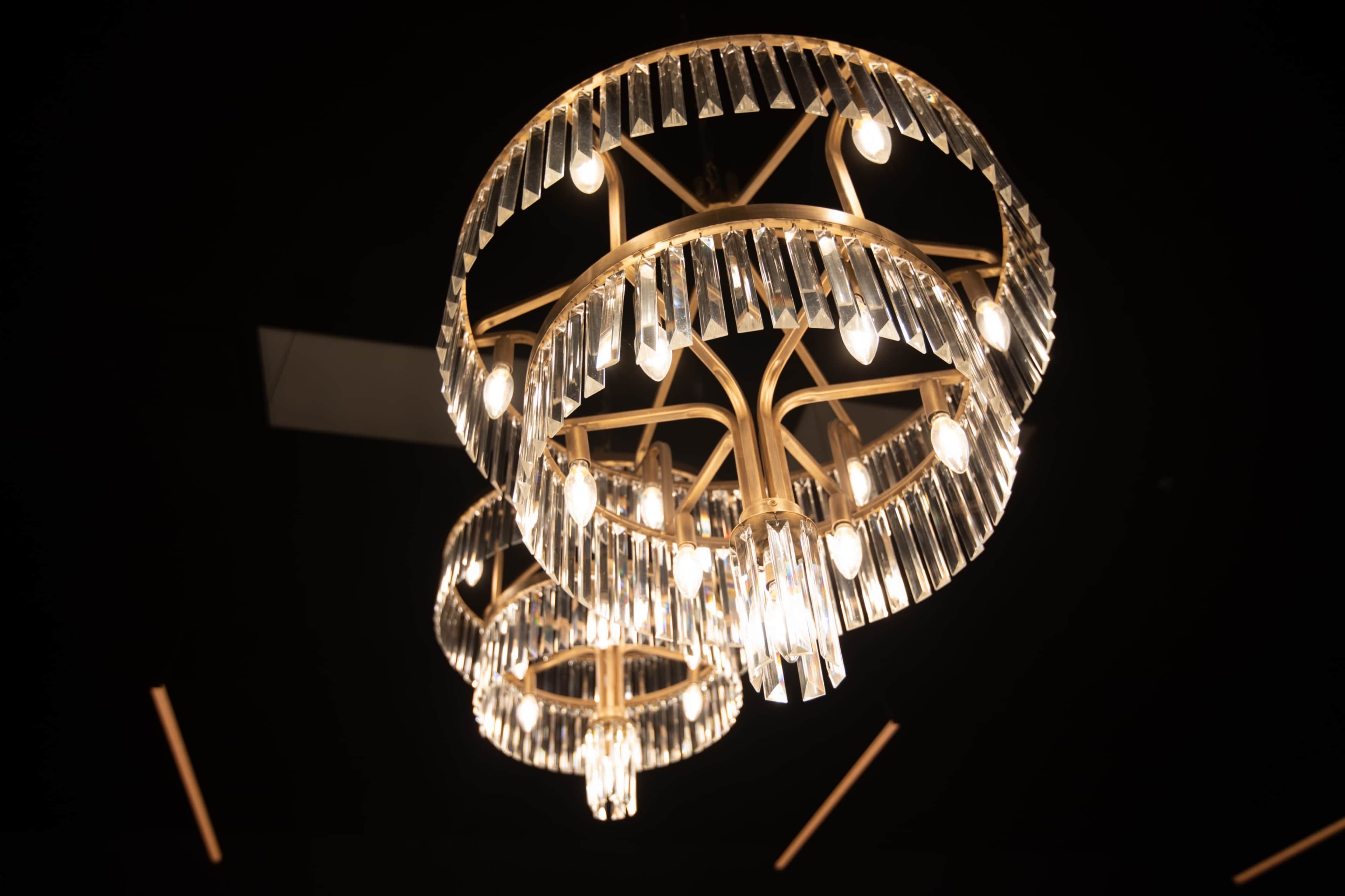 Two elegant chandeliers with crystal accents and multiple light bulbs, suspended from a dark ceiling.