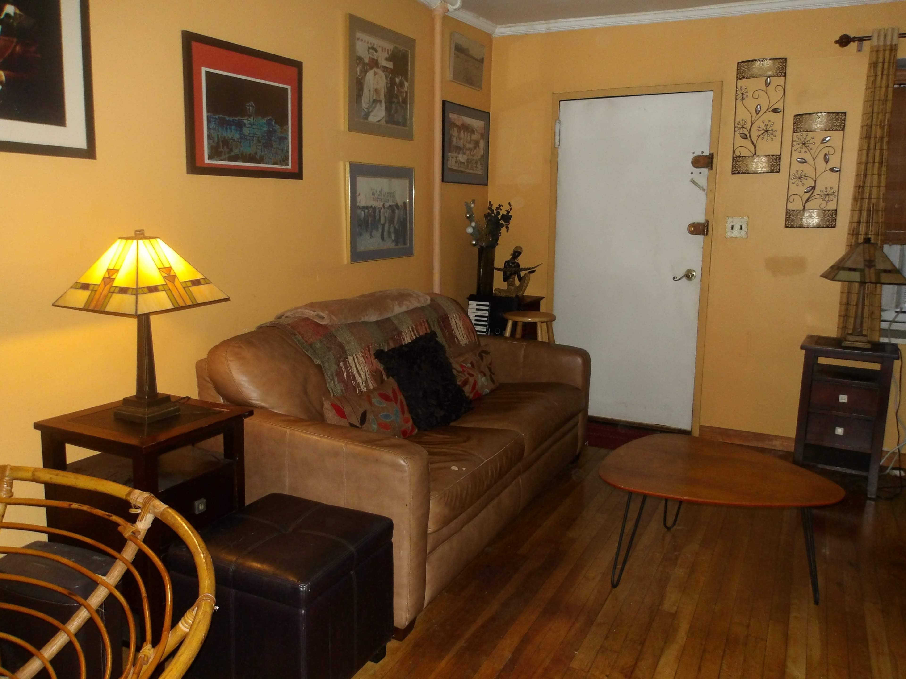 The room features a brown leather sofa, a wooden coffee table, and a variety of framed artwork on the walls.
