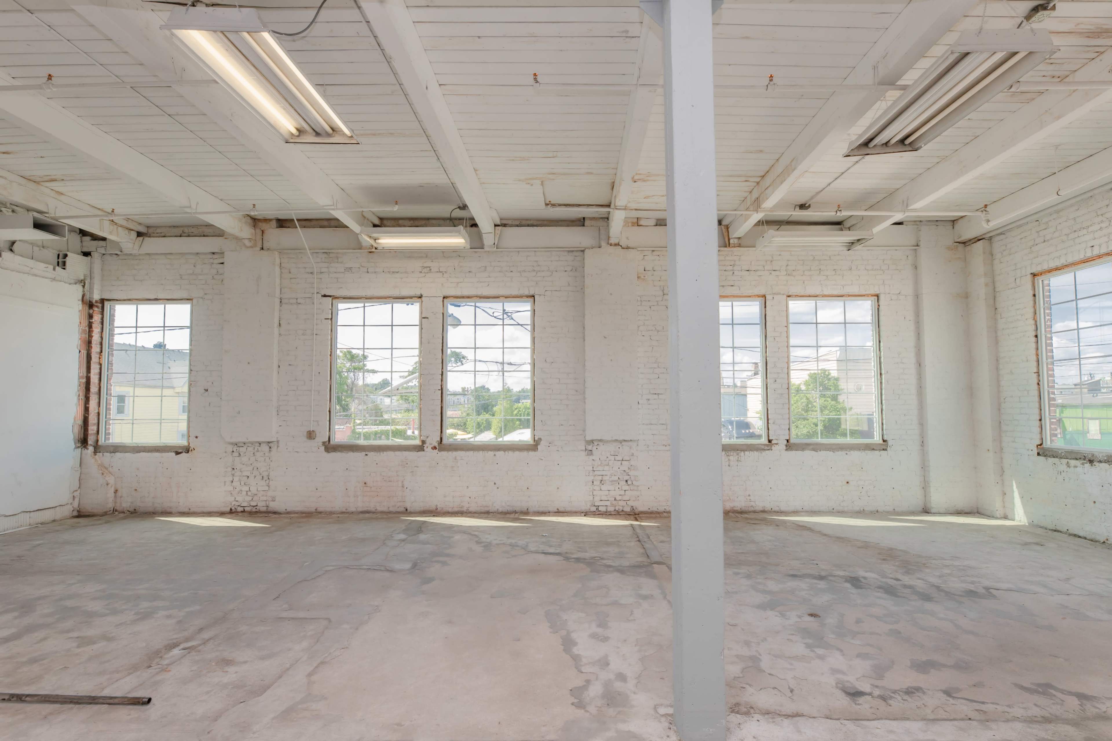 An empty, bright room with large windows and exposed brick walls.