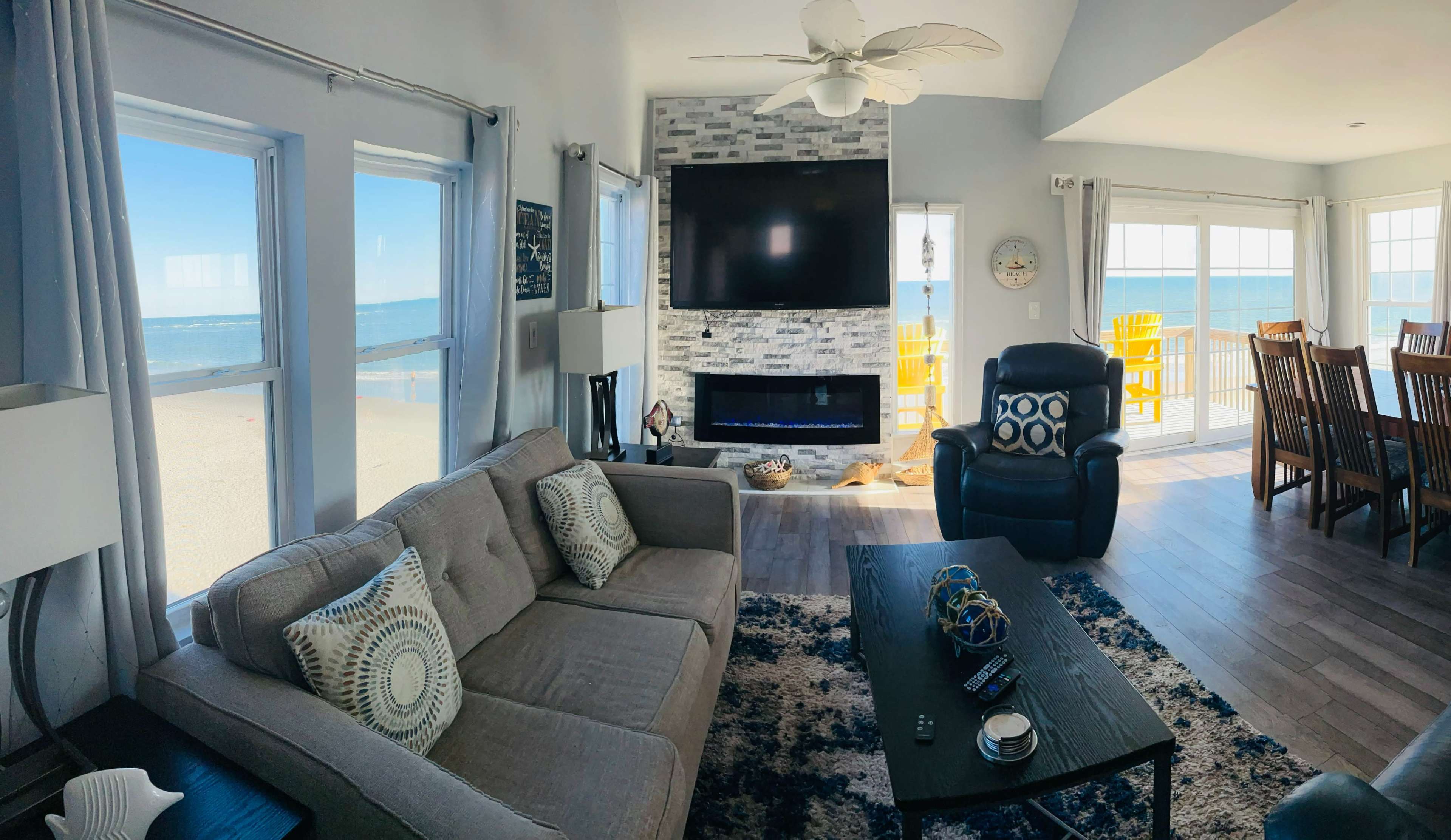 A coastal living room with a sectional sofa, a modern fireplace, and large windows revealing a view of the beach and ocean.
