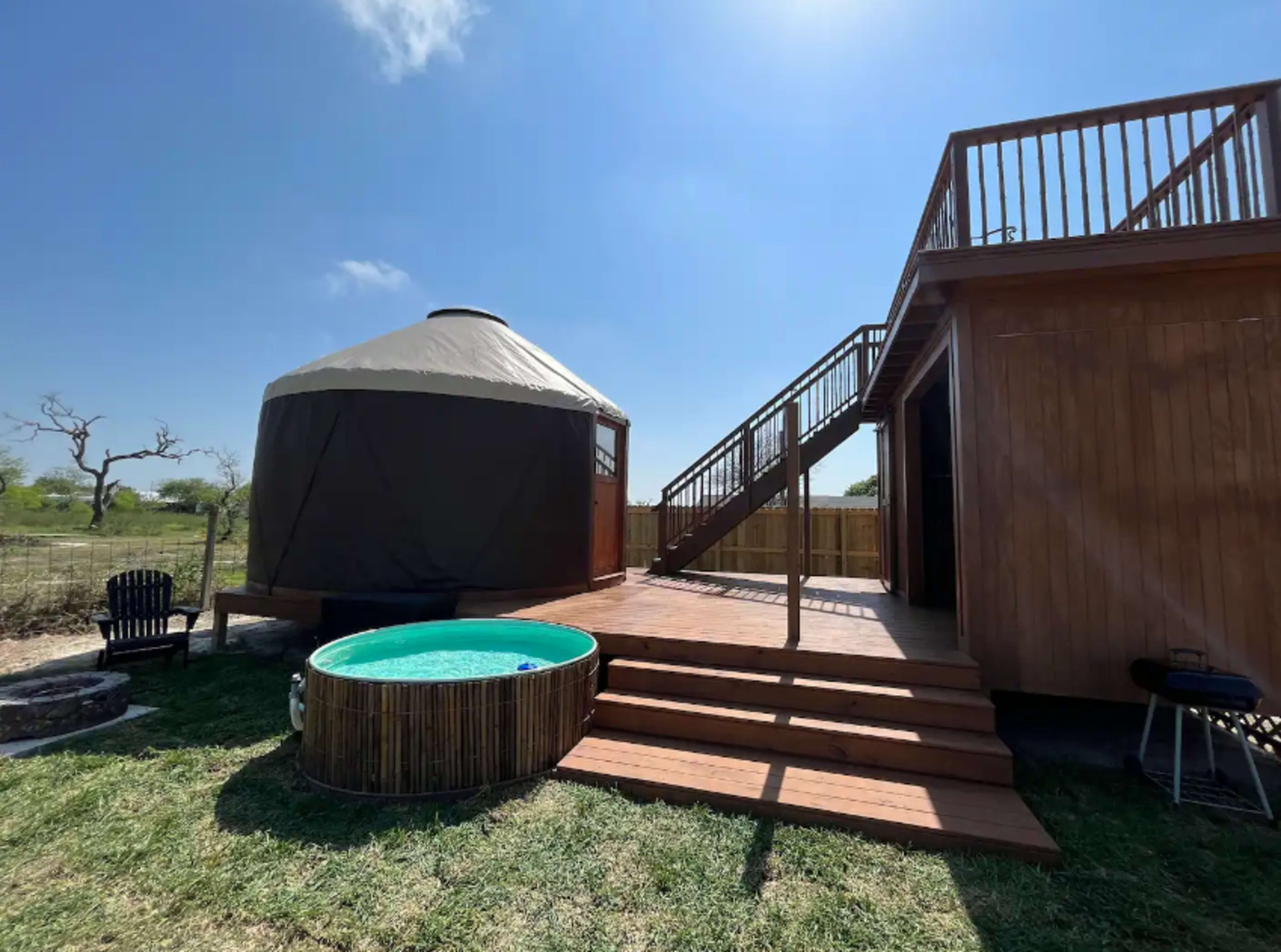 A wooden deck leading to a round yurt with a hot tub beside it and stairs leading to an upper level.