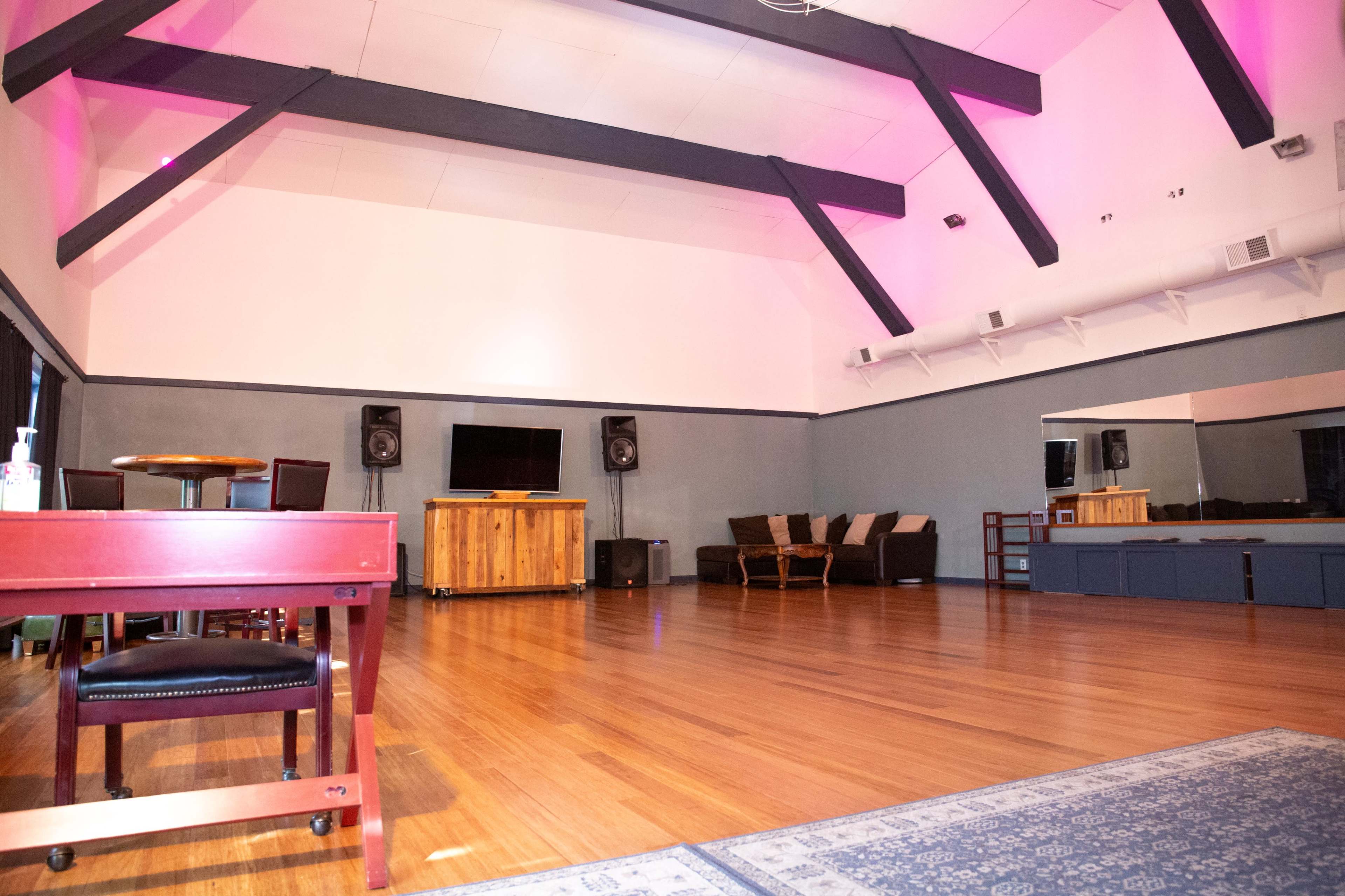 The spacious interior features a wooden floor, high ceilings with exposed beams, a seating area, and audio equipment.