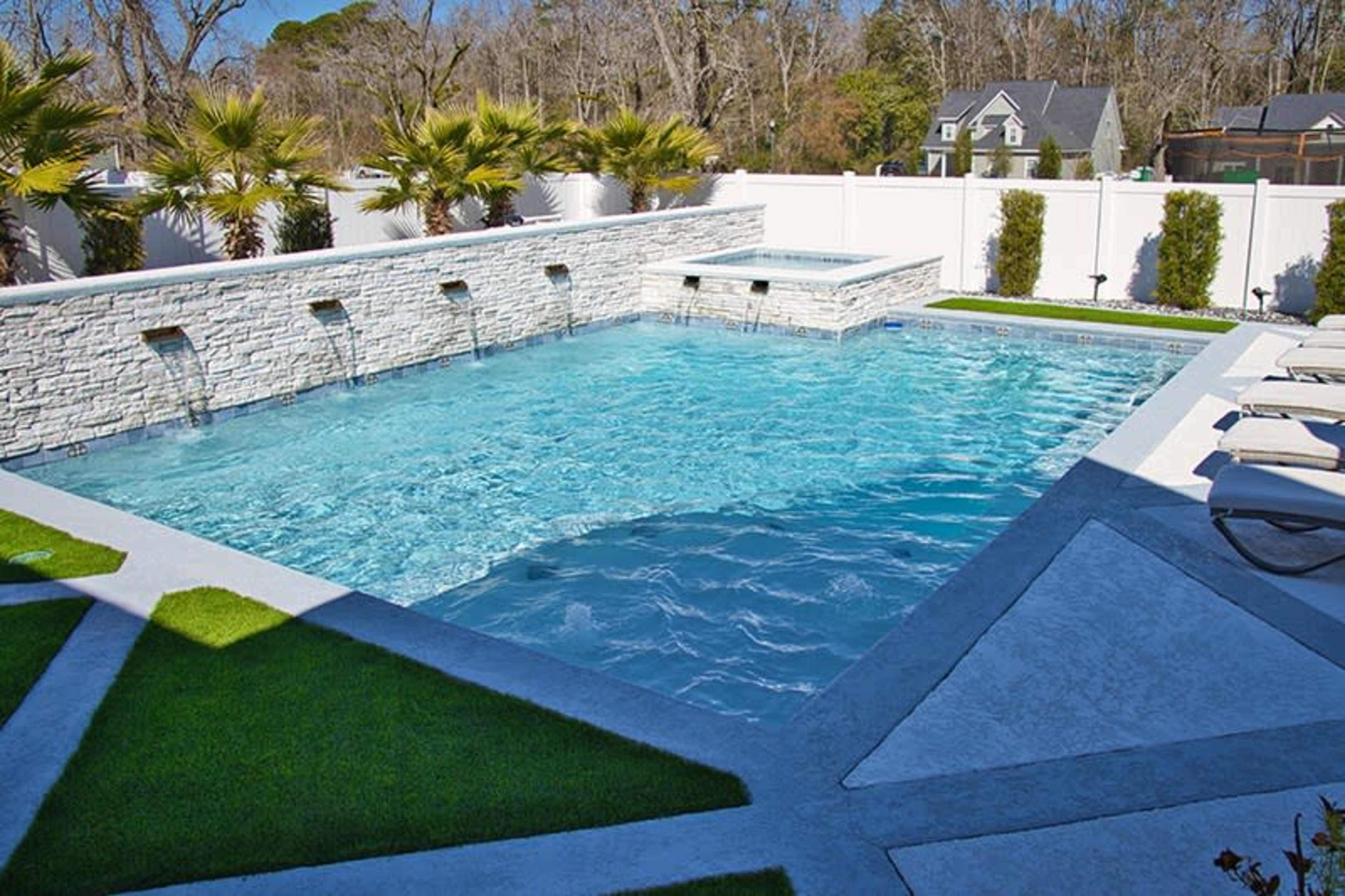 A rectangular swimming pool with a stone wall fountain, surrounded by clean landscaping and a spa area.